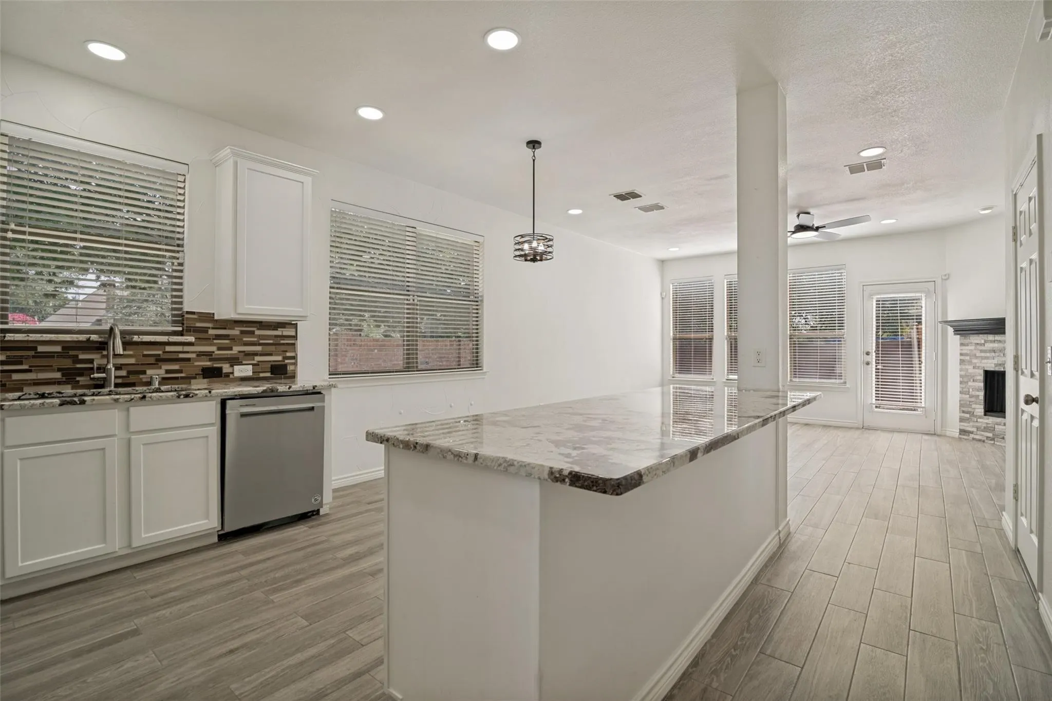 Kitchen with wood-finish flooring, white cabinetry, a large center island with a light-colored countertop, and a mosaic tile backsplash