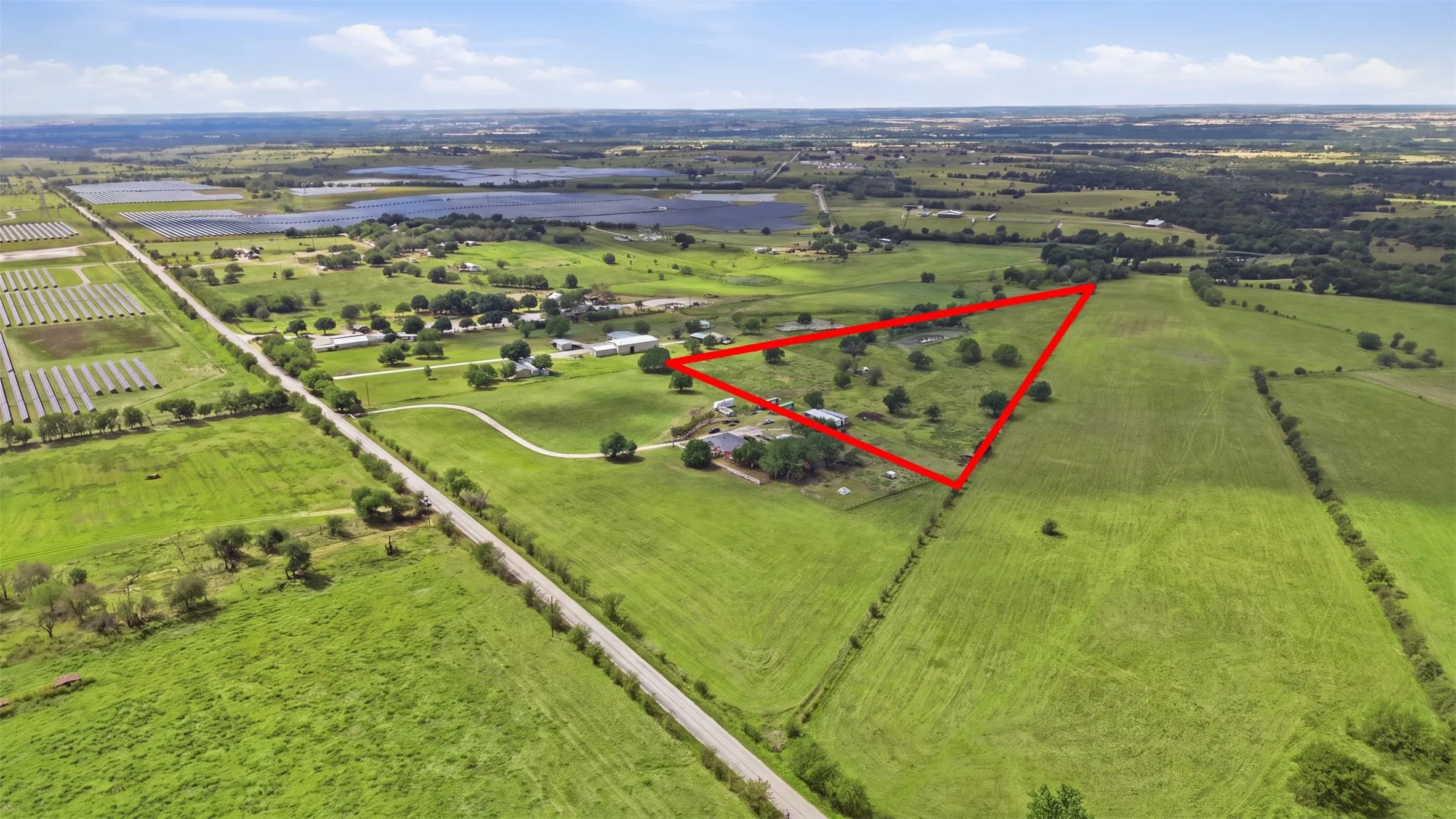 Expansive agricultural property featuring a dwelling, a winding driveway, mature trees, and a surrounding green landscape