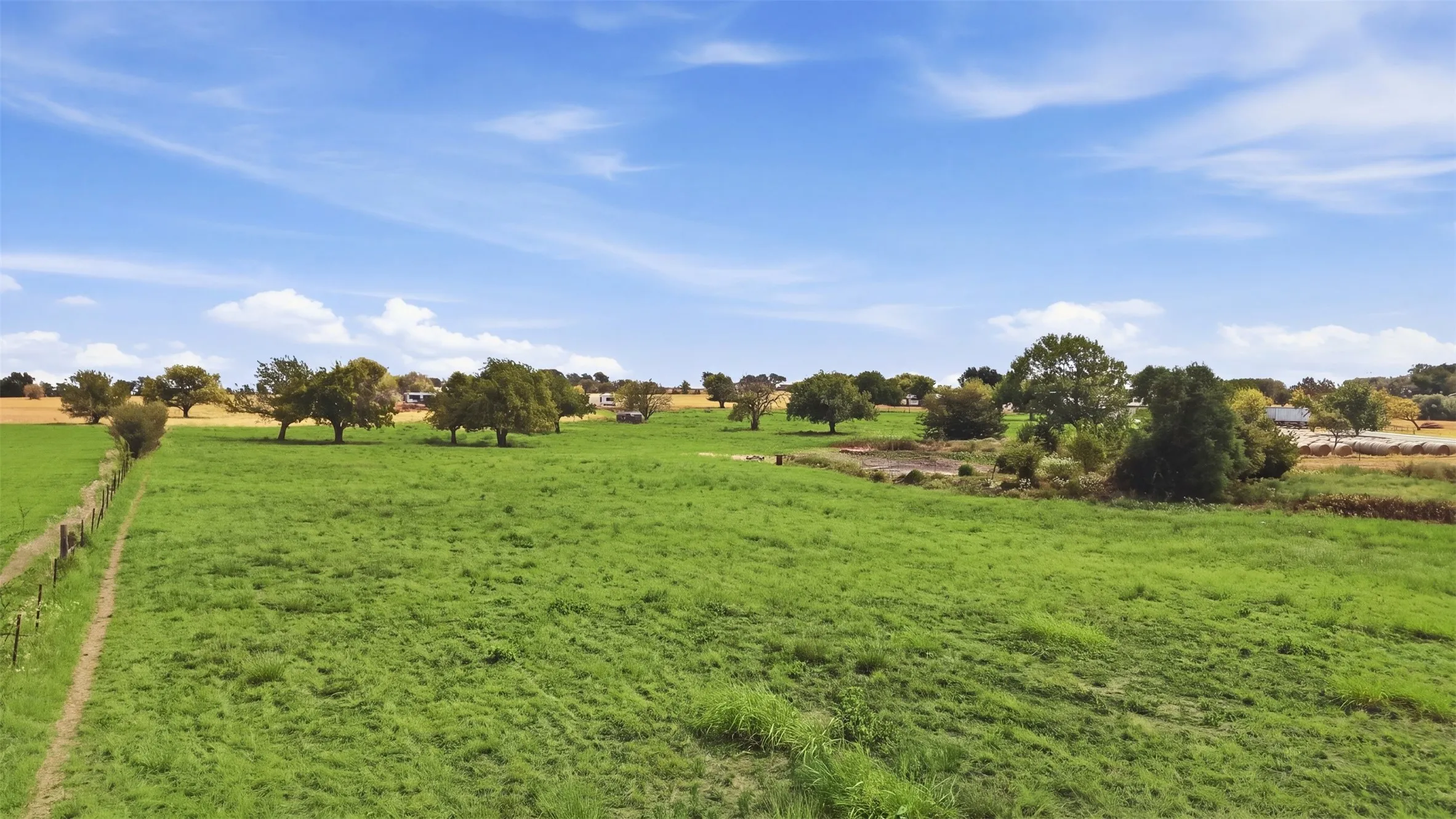 Expansive green pastureland with mature trees and perimeter fencing
