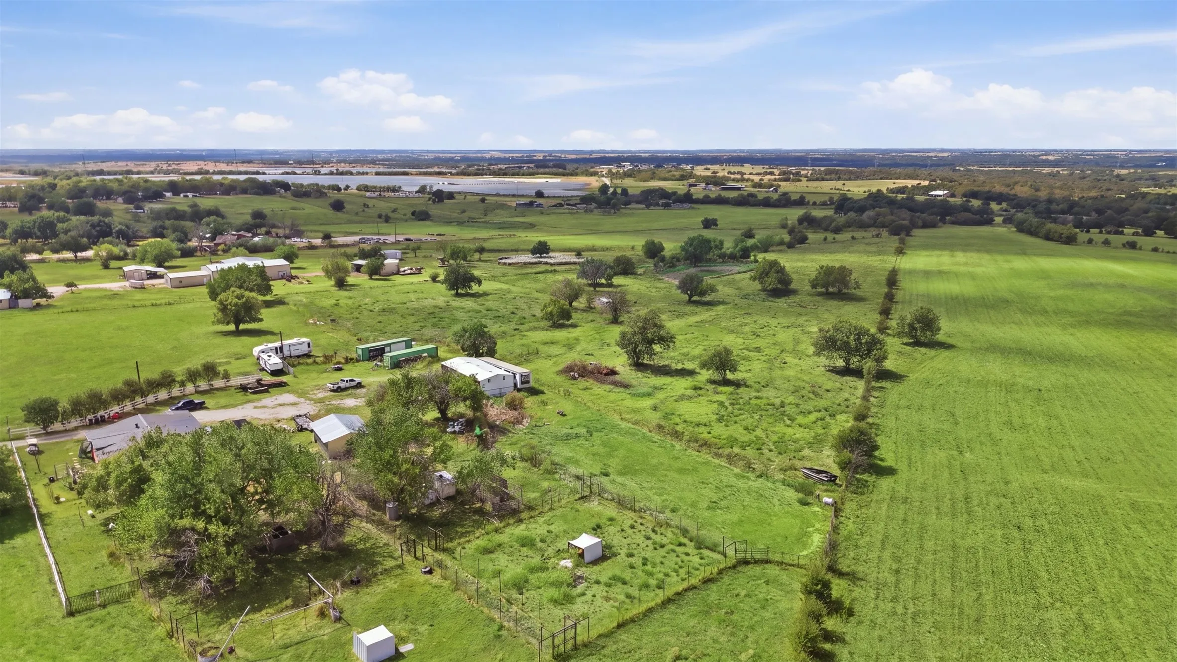 Expansive green acreage with scattered mature trees and a distant body of water