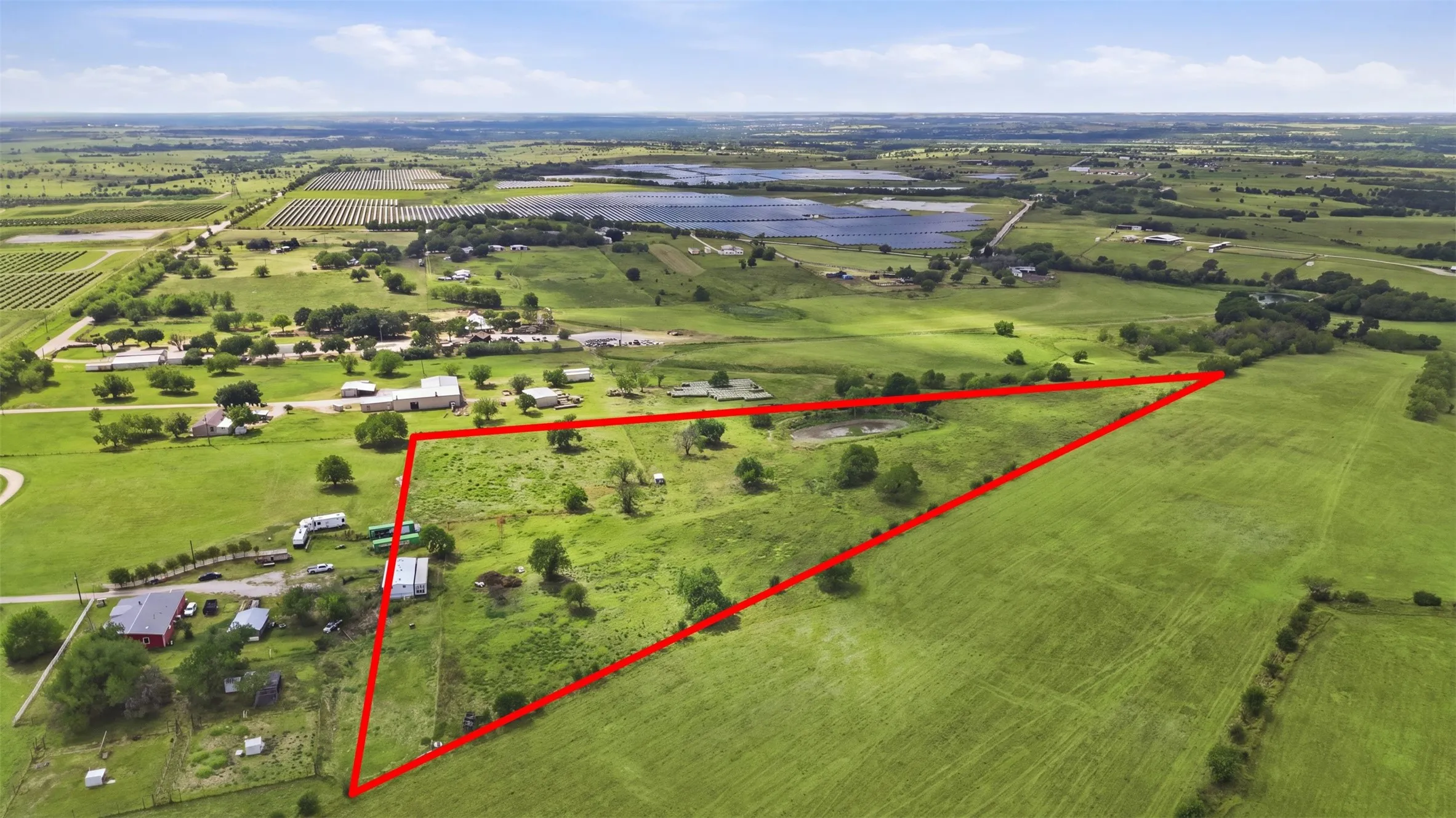 Expansive green acreage with a distinct red boundary, featuring scattered trees and a natural pond