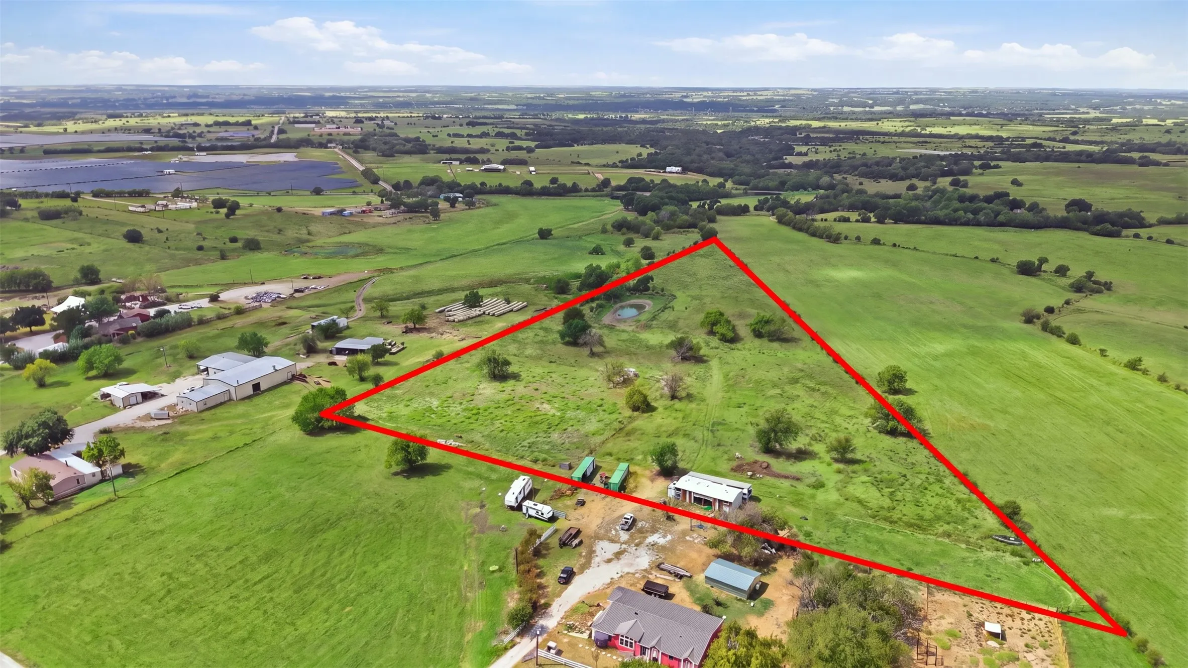 Expansive parcel featuring a triangular boundary, a natural pond, and mature trees, surrounded by open green fields