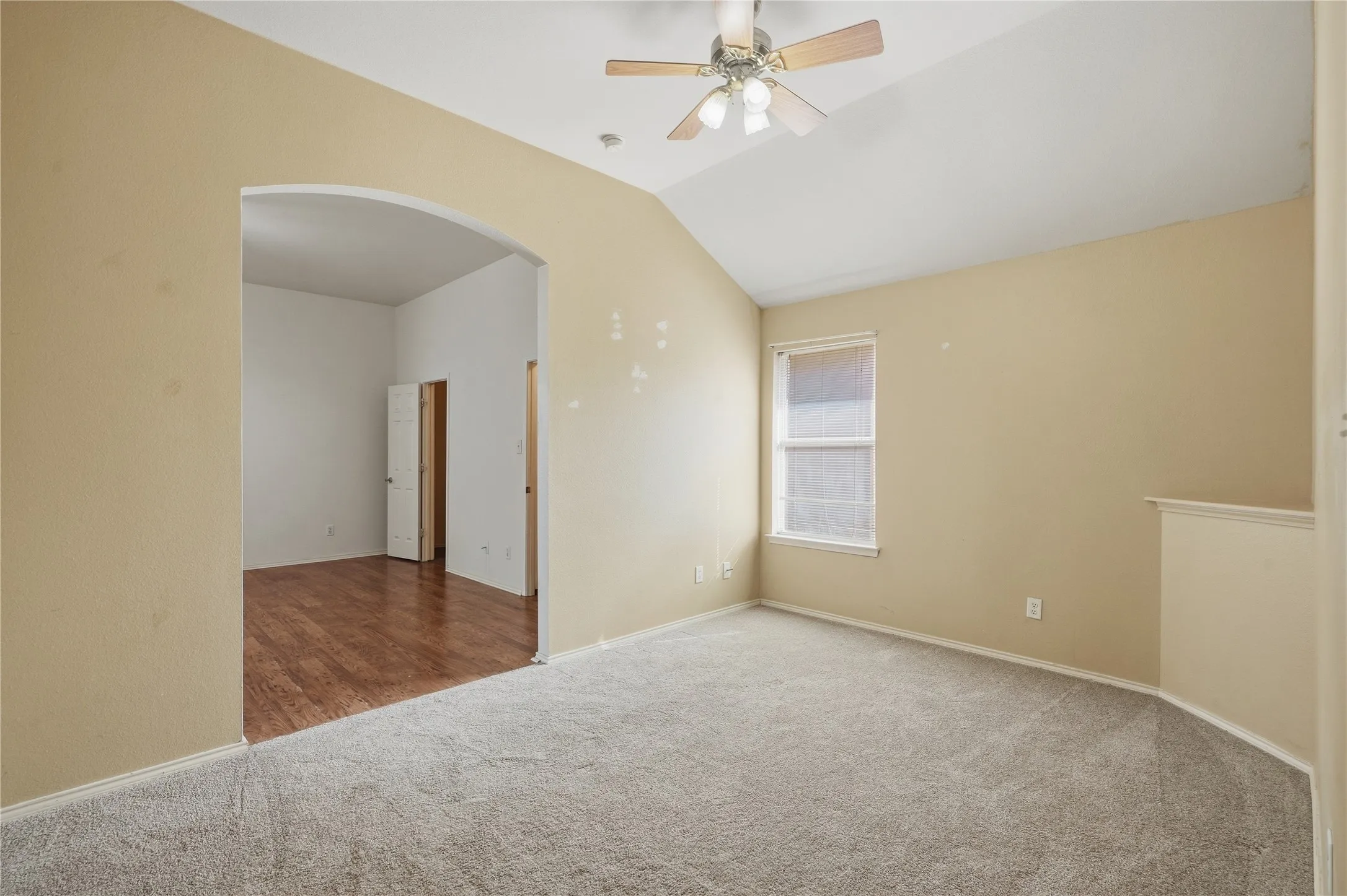 Vaulted ceiling with an attached ceiling fan, arched doorway, window with blinds, and carpeted flooring