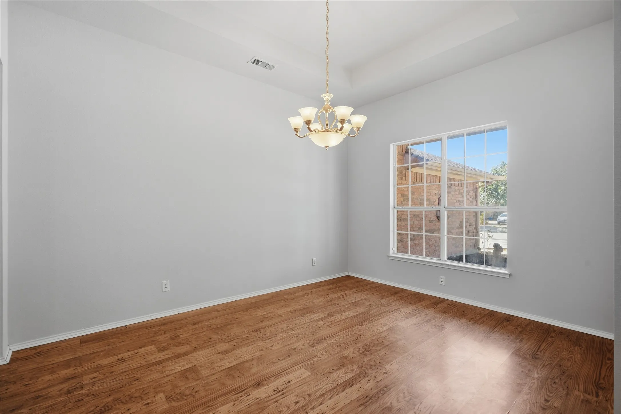 Wood-finish flooring, tray ceiling, multi-pane window, and a chandelier with glass shades