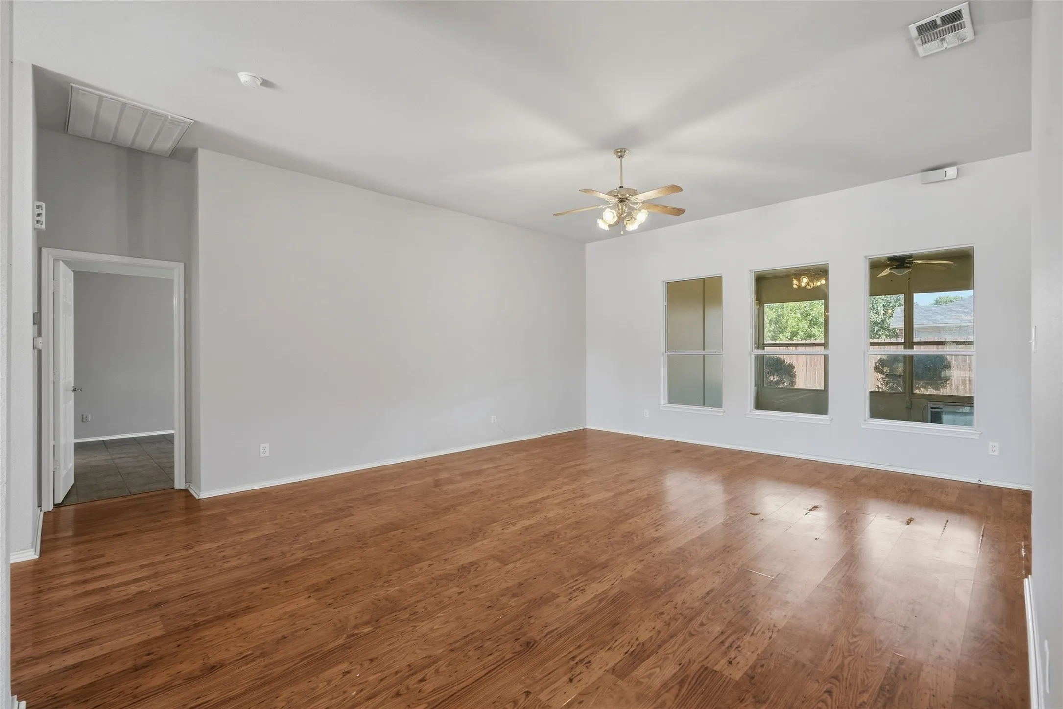 Spacious interior with wood-finish flooring, light gray wall paint, a ceiling fan with integrated lighting, and multiple windows