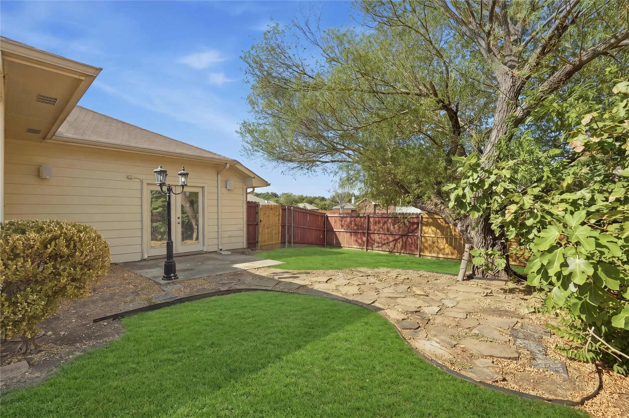 Expansive backyard with a manicured lawn, flagstone pathway, mature shade tree, and wood fencing