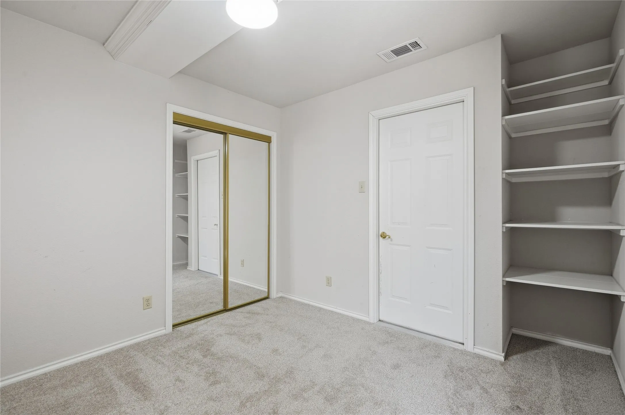 Light gray carpeted flooring, mirrored sliding closet doors, built-in shelving, white paneled door, and recessed lighting