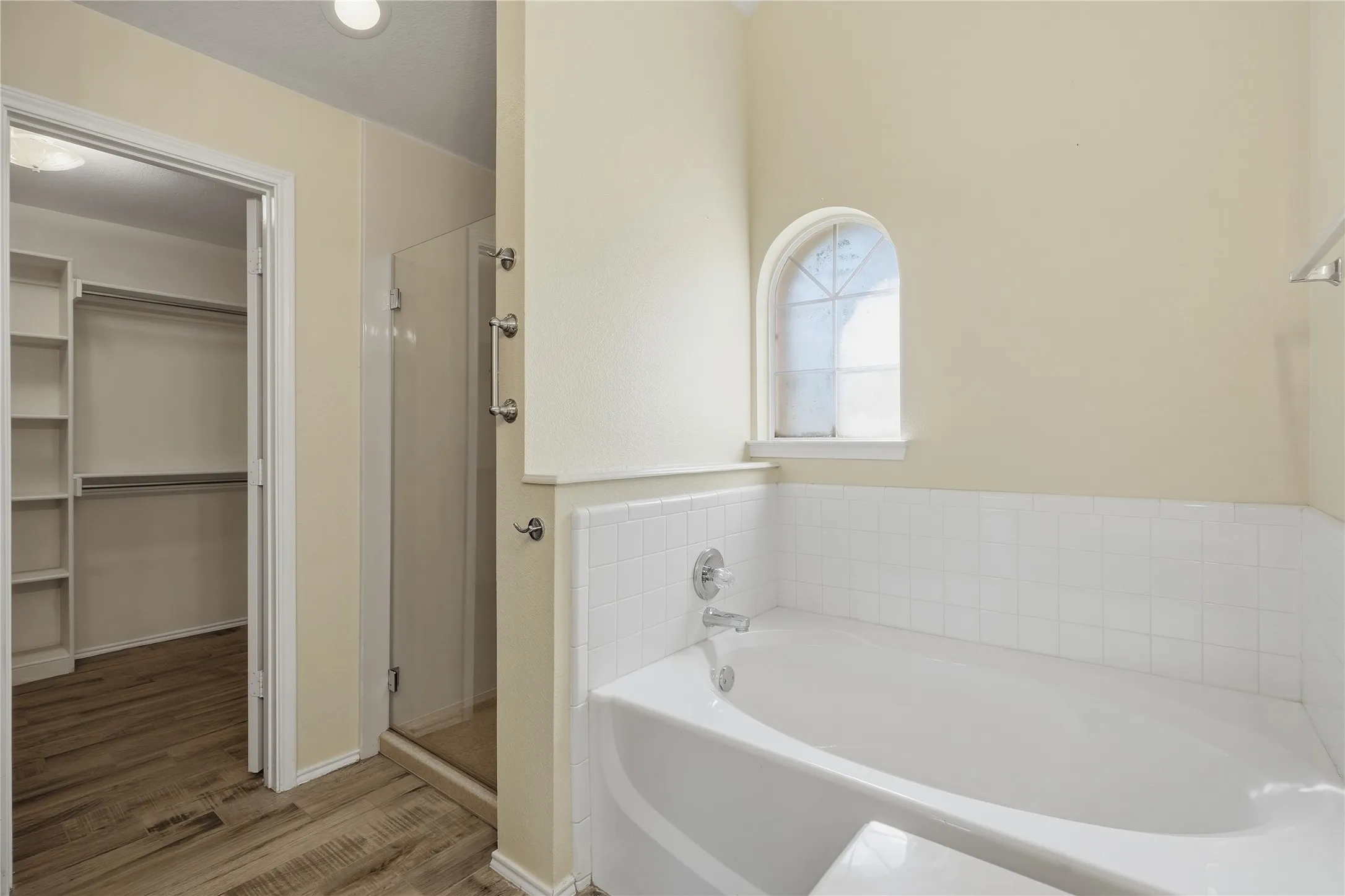Soaking tub with white tile surround, arched window, and chrome fixtures