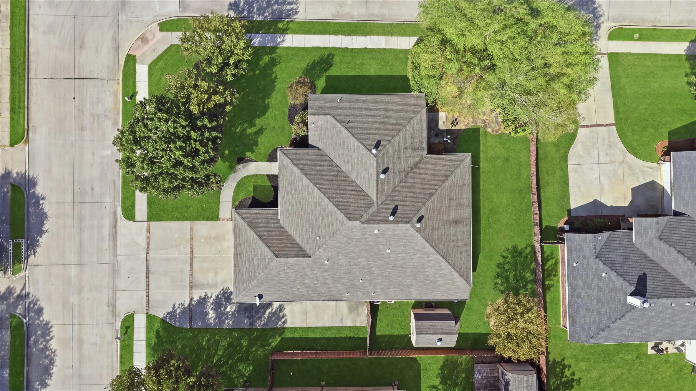 Corner lot with concrete driveway, mature landscaping, and a detached shed