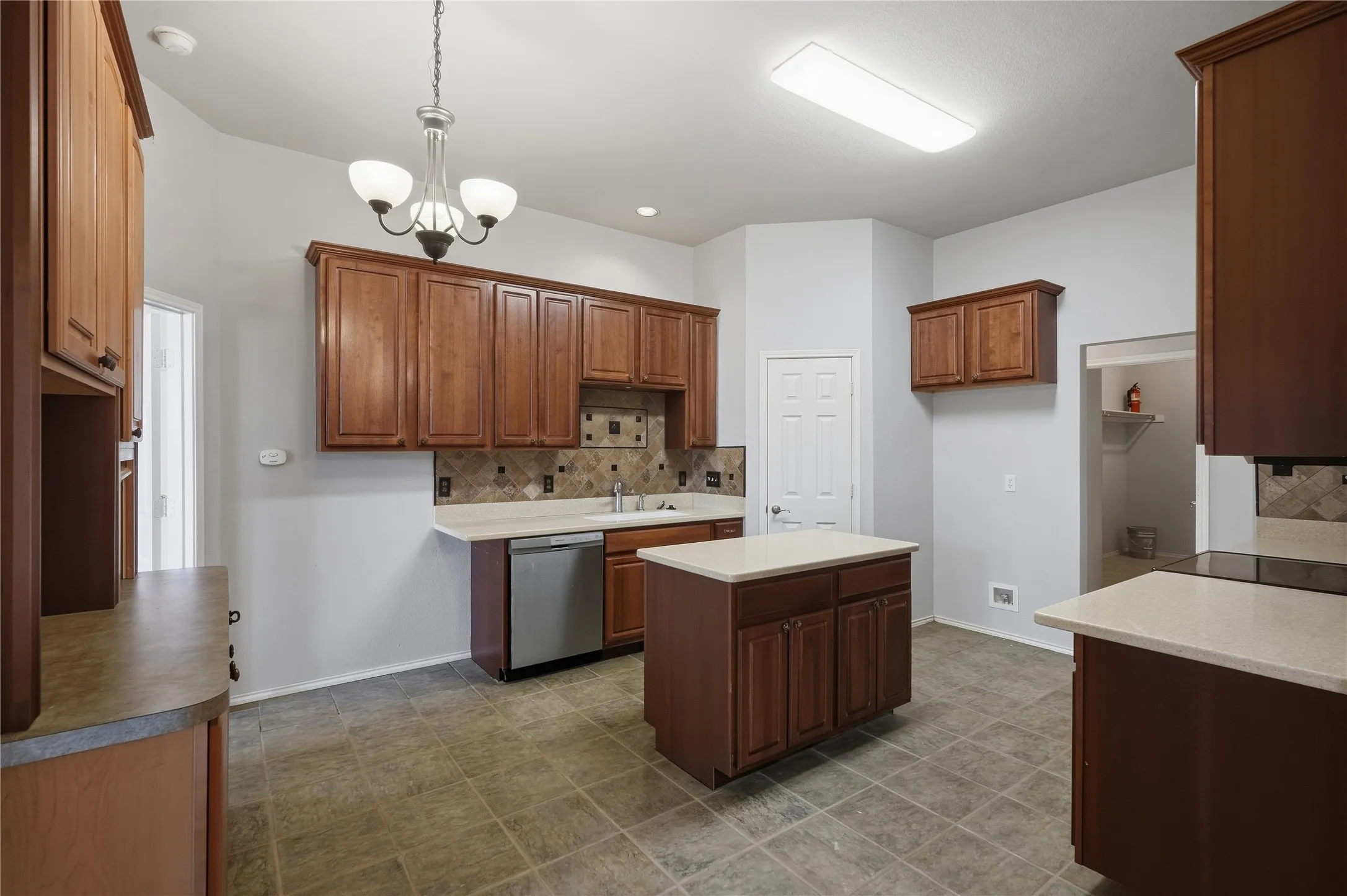 Kitchen featuring wood cabinetry, light countertops, a central island, stainless steel dishwasher, and tile flooring