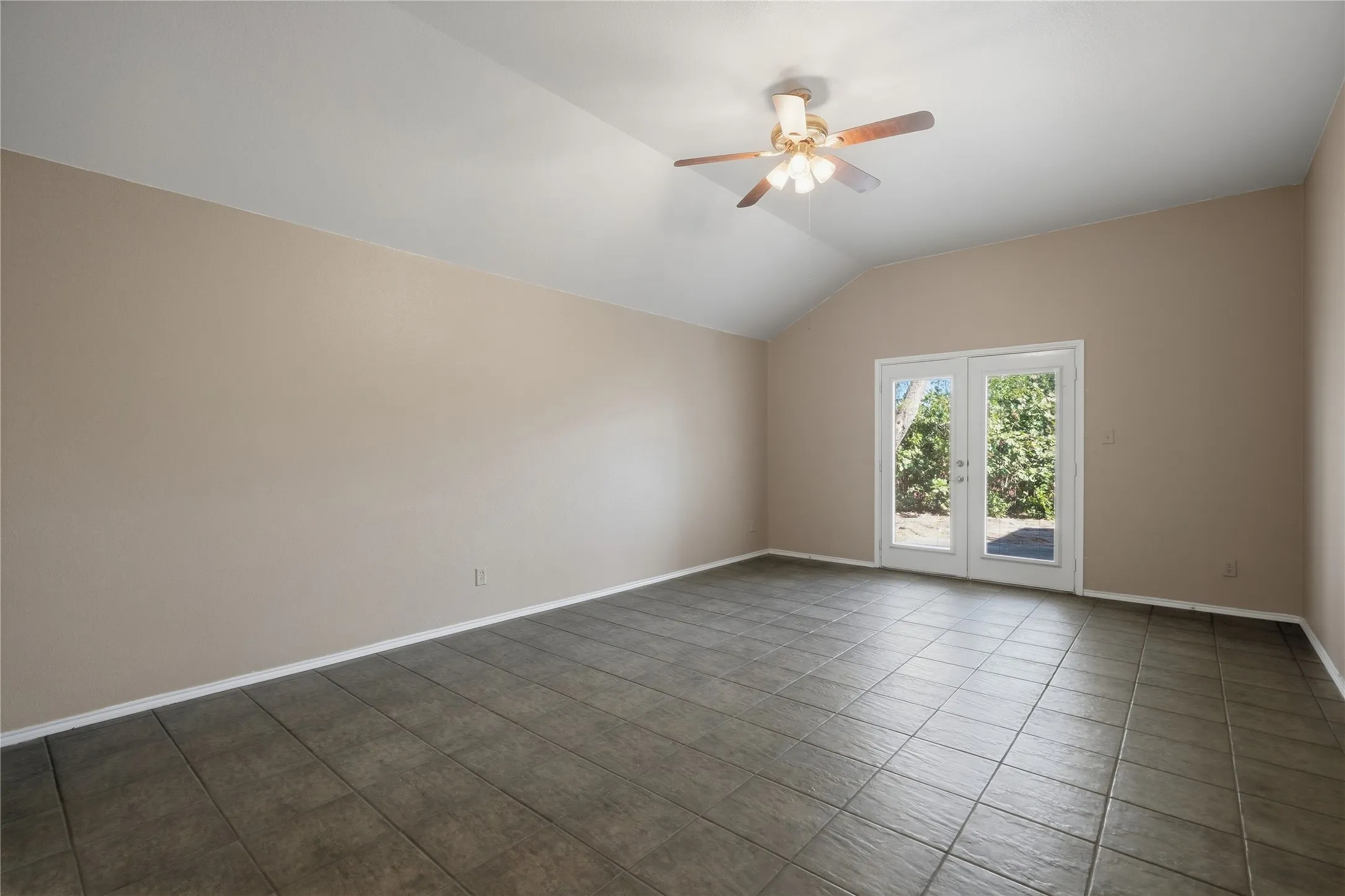 Vaulted ceiling with an attached ceiling fan, dual-pane French doors, and tile flooring
