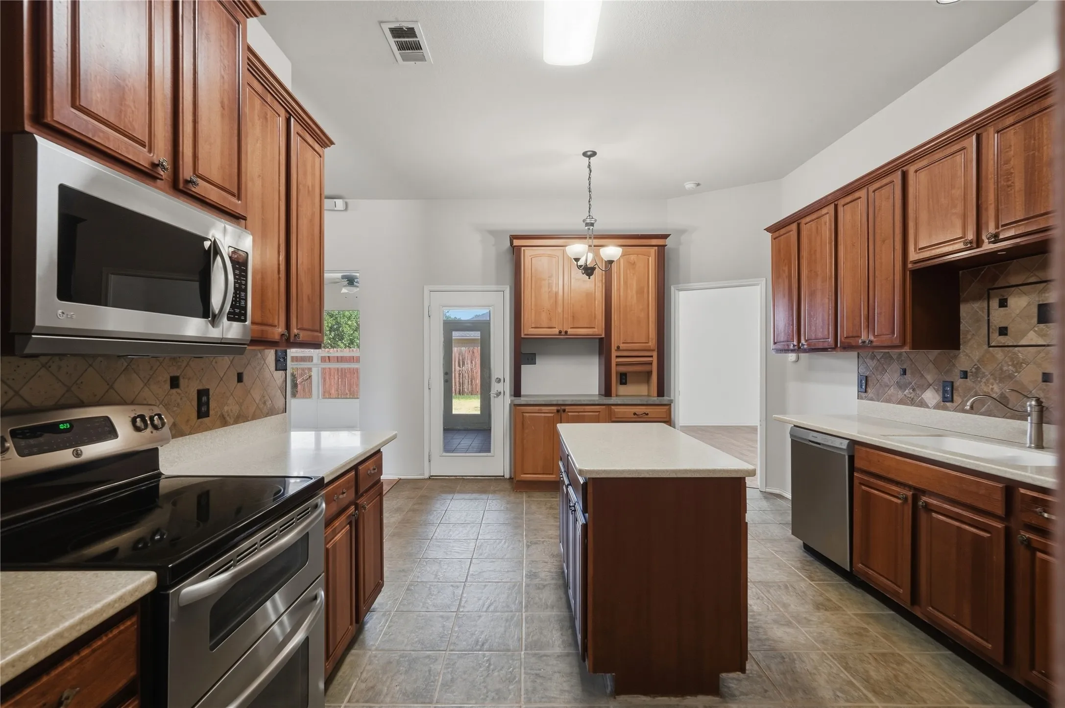 Kitchen featuring wood cabinetry, stainless steel appliances, a center island with countertop, tile flooring, and a tiled backsplash