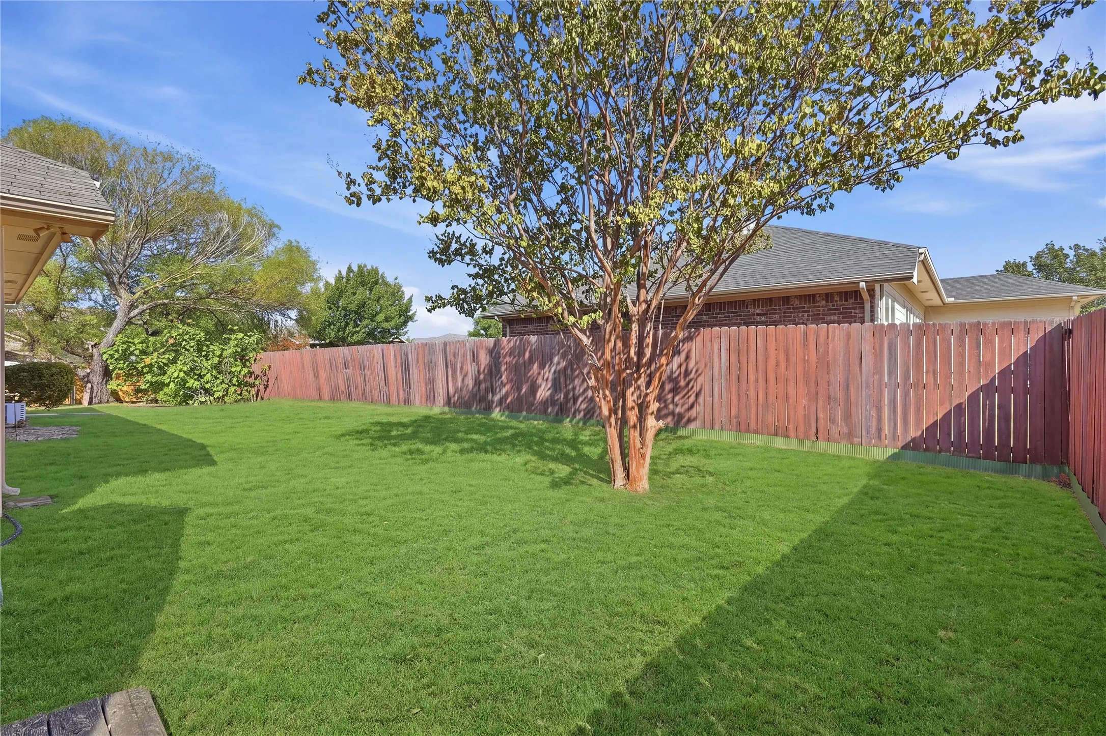 Expansive lawn area with a mature tree, bordered by a privacy fence, and partial view of the home's exterior