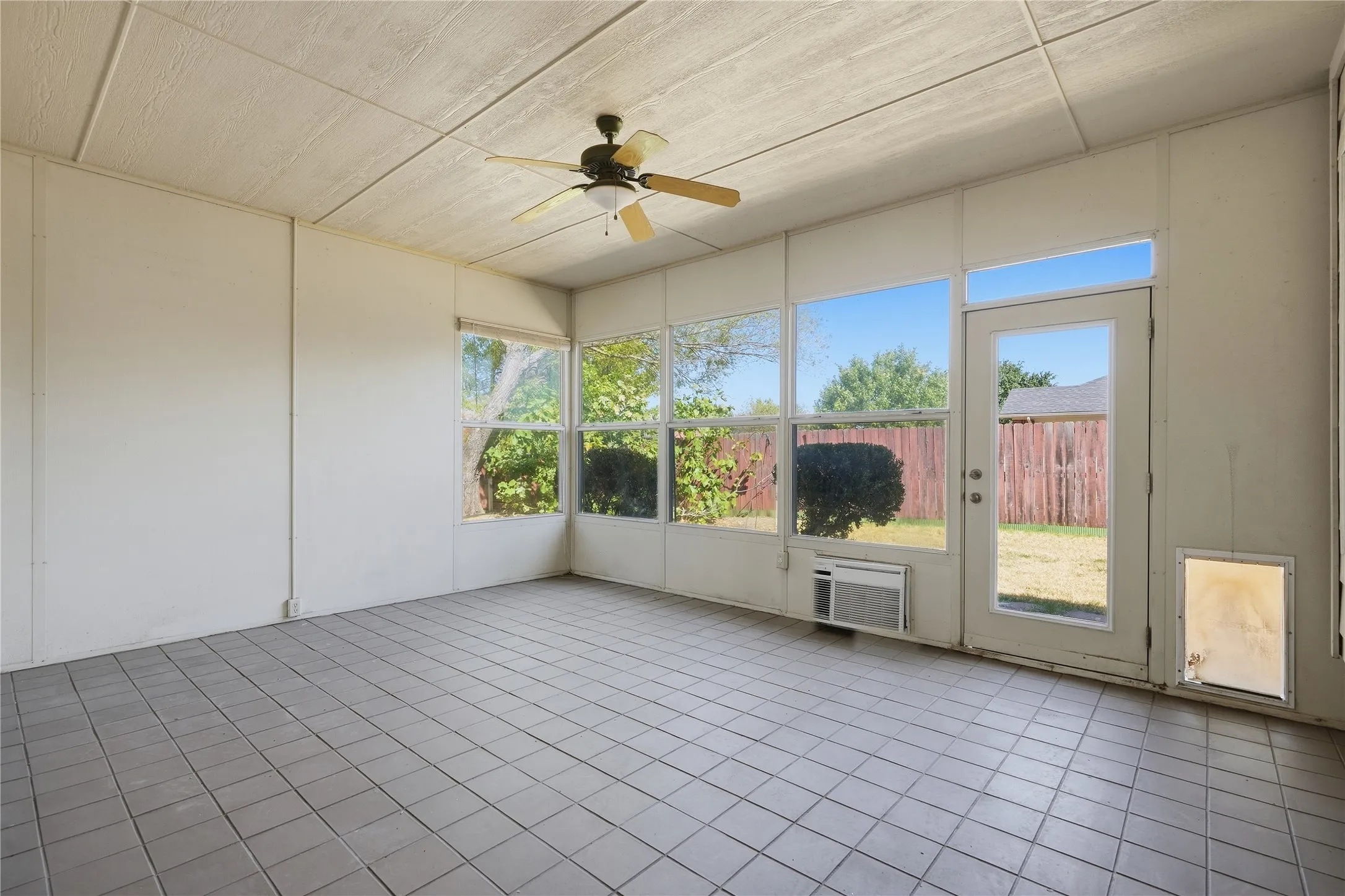 Sunroom featuring tile flooring, multiple windows, an exterior door, and a ceiling fan