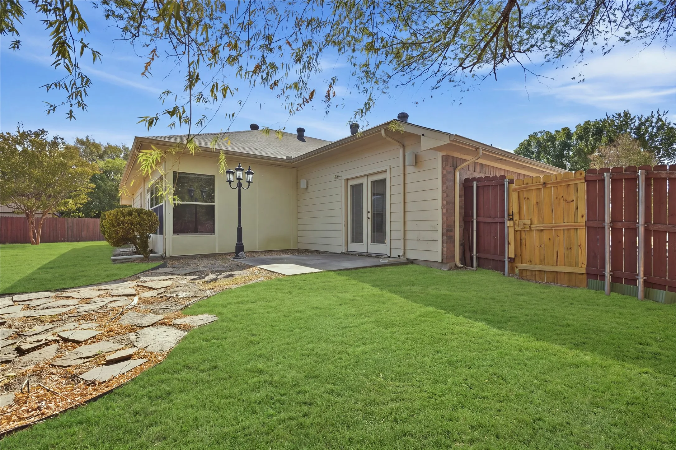 Expansive lawn area with a flagstone pathway, a concrete patio, and a privacy fence