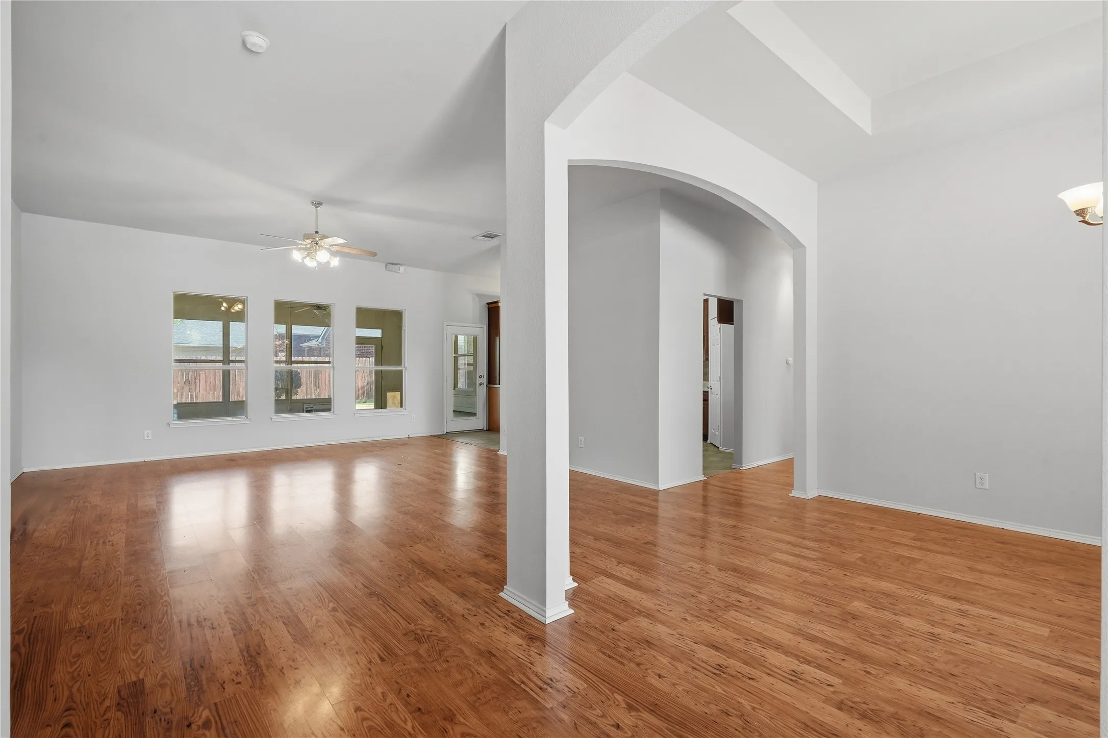 Wood-finish flooring throughout, multiple windows, archway entry, and ceiling fan with integrated lighting
