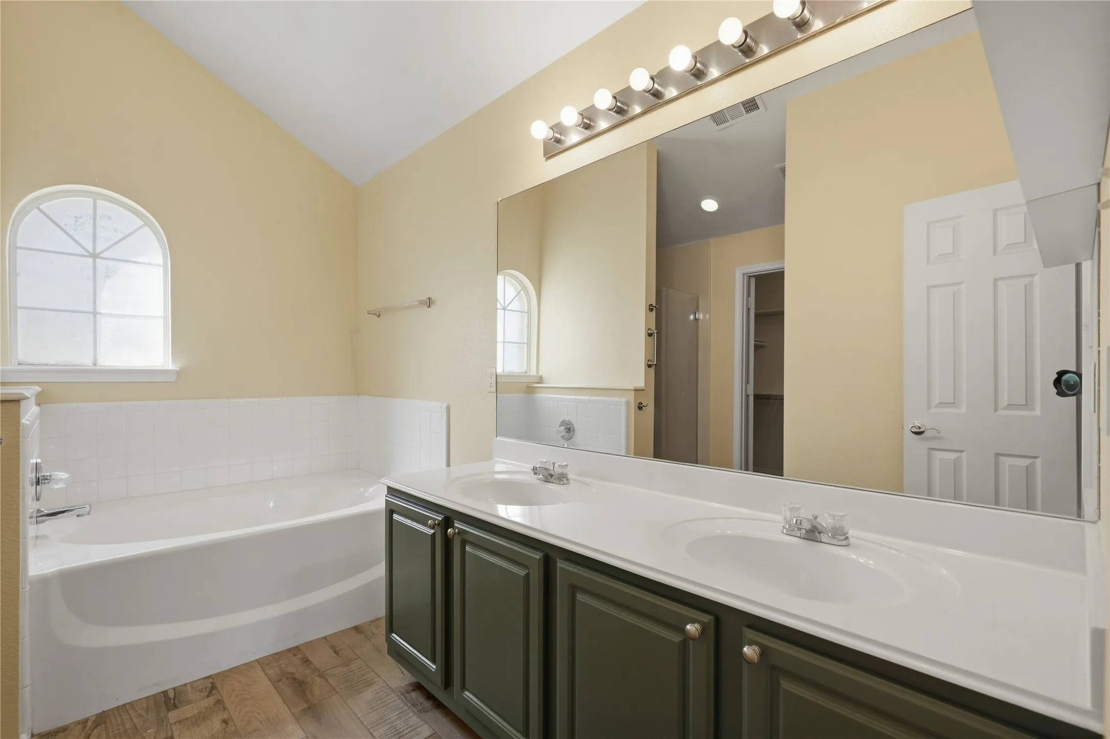 Dual sink vanity with dark-finish cabinetry, a large integrated mirror, and a built-in bathtub with a tiled surround