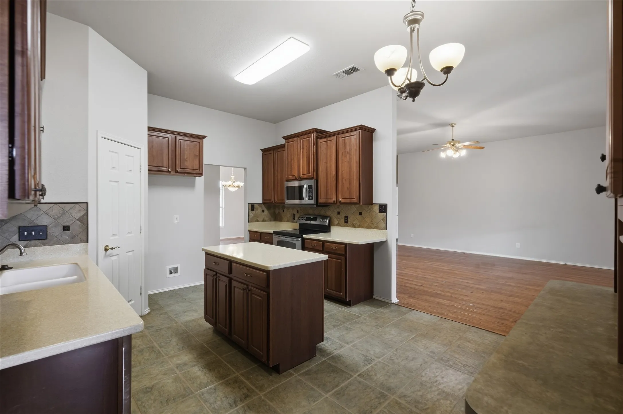 Kitchen featuring a central island, wood-finish cabinetry, light-toned countertops, tile flooring, and stainless steel appliances