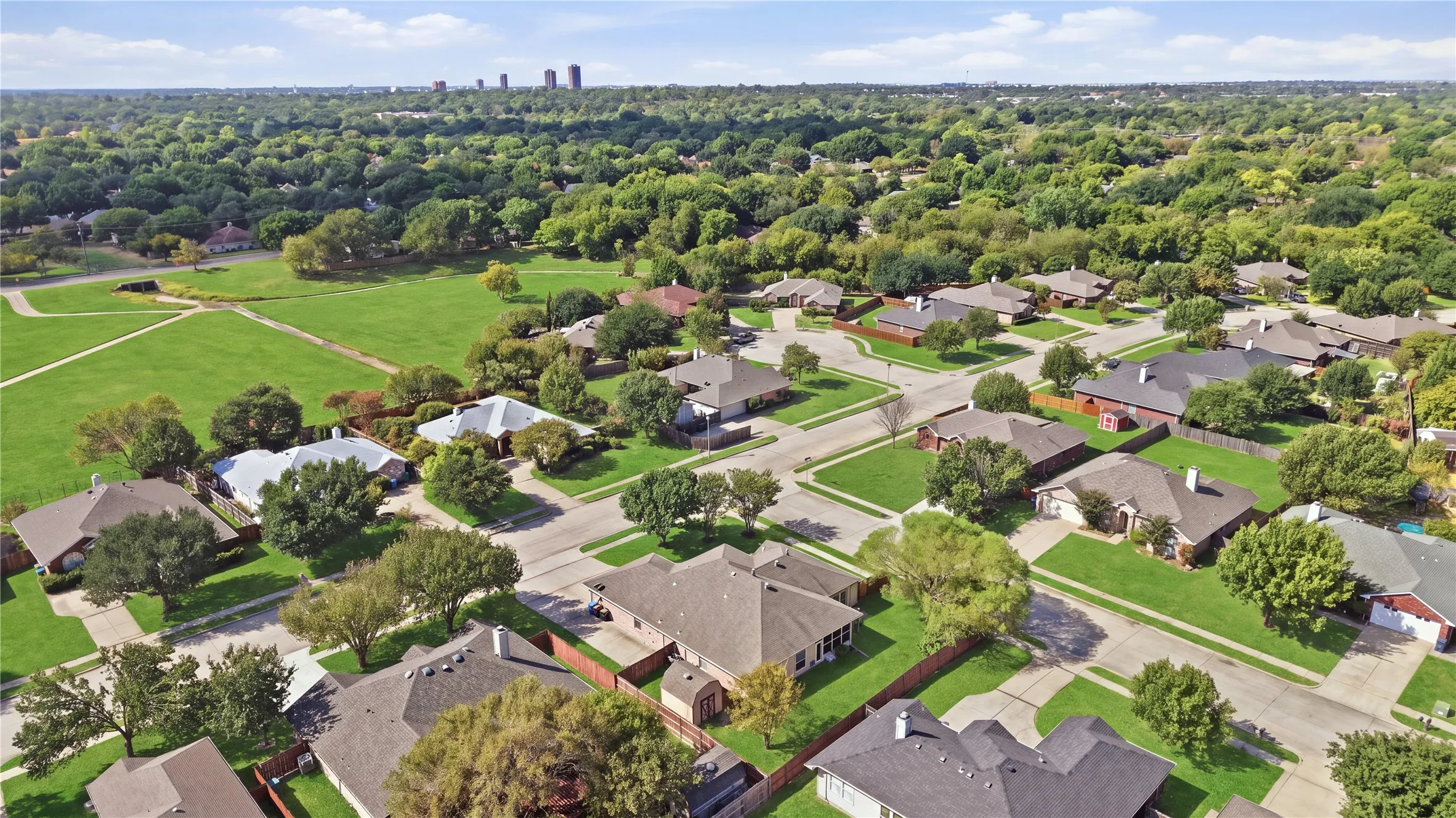 Expansive green spaces and mature trees surround residential properties, featuring paved streets and varied rooflines