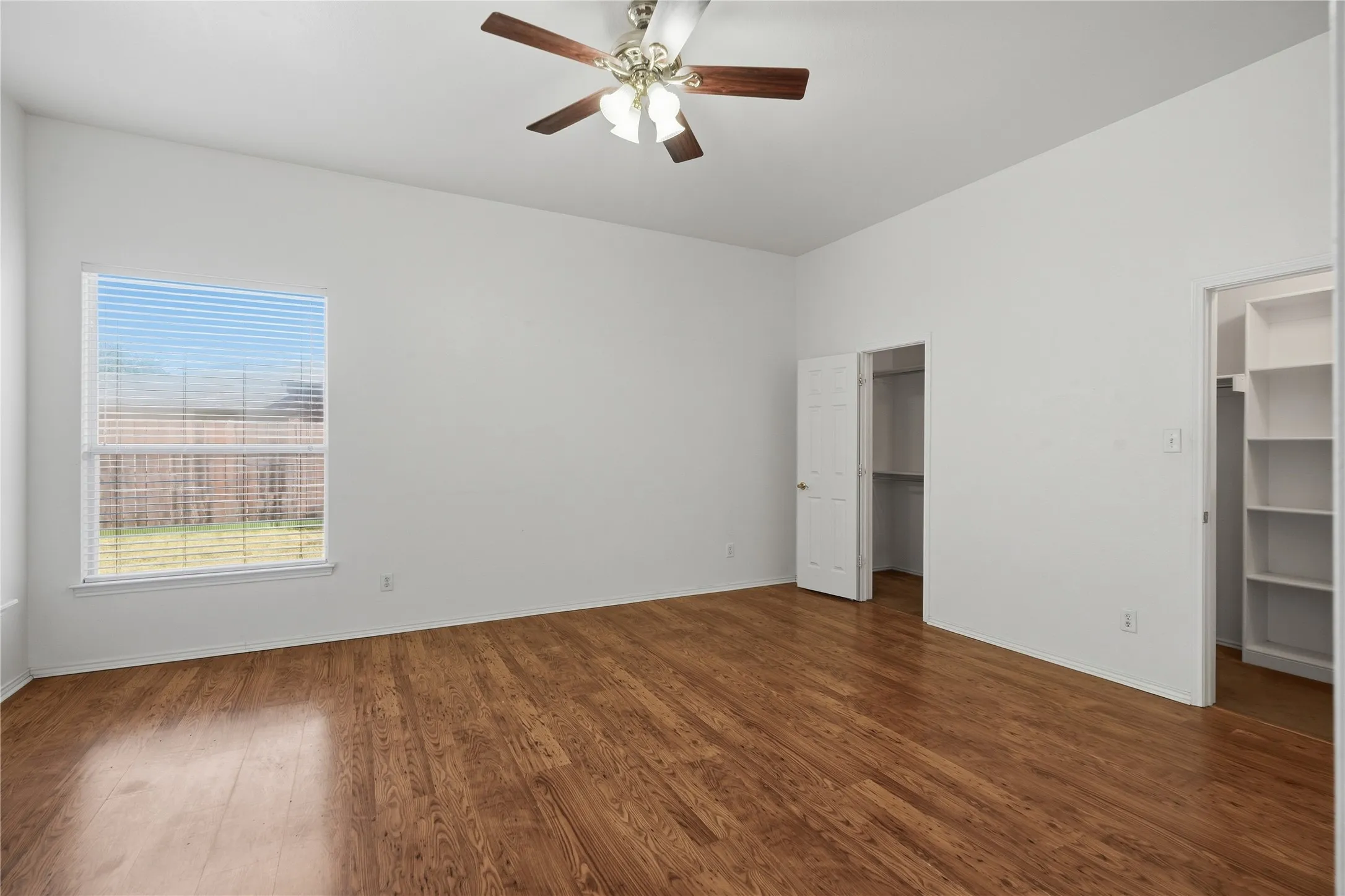 Spacious room featuring wood-finish flooring, a ceiling fan, and two closet spaces with built-in shelving