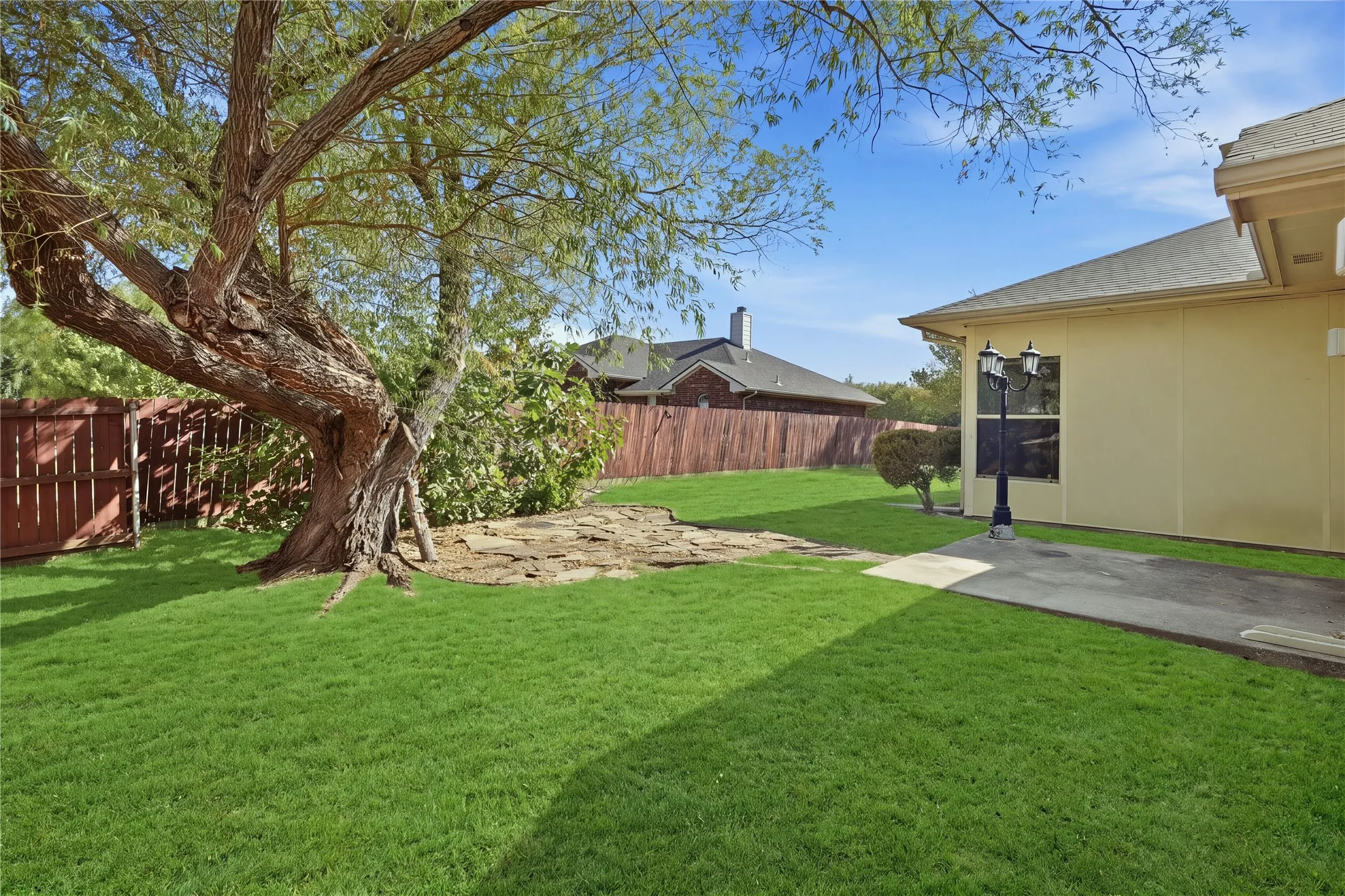 Expansive backyard featuring a manicured lawn, established tree, concrete patio, and privacy fencing