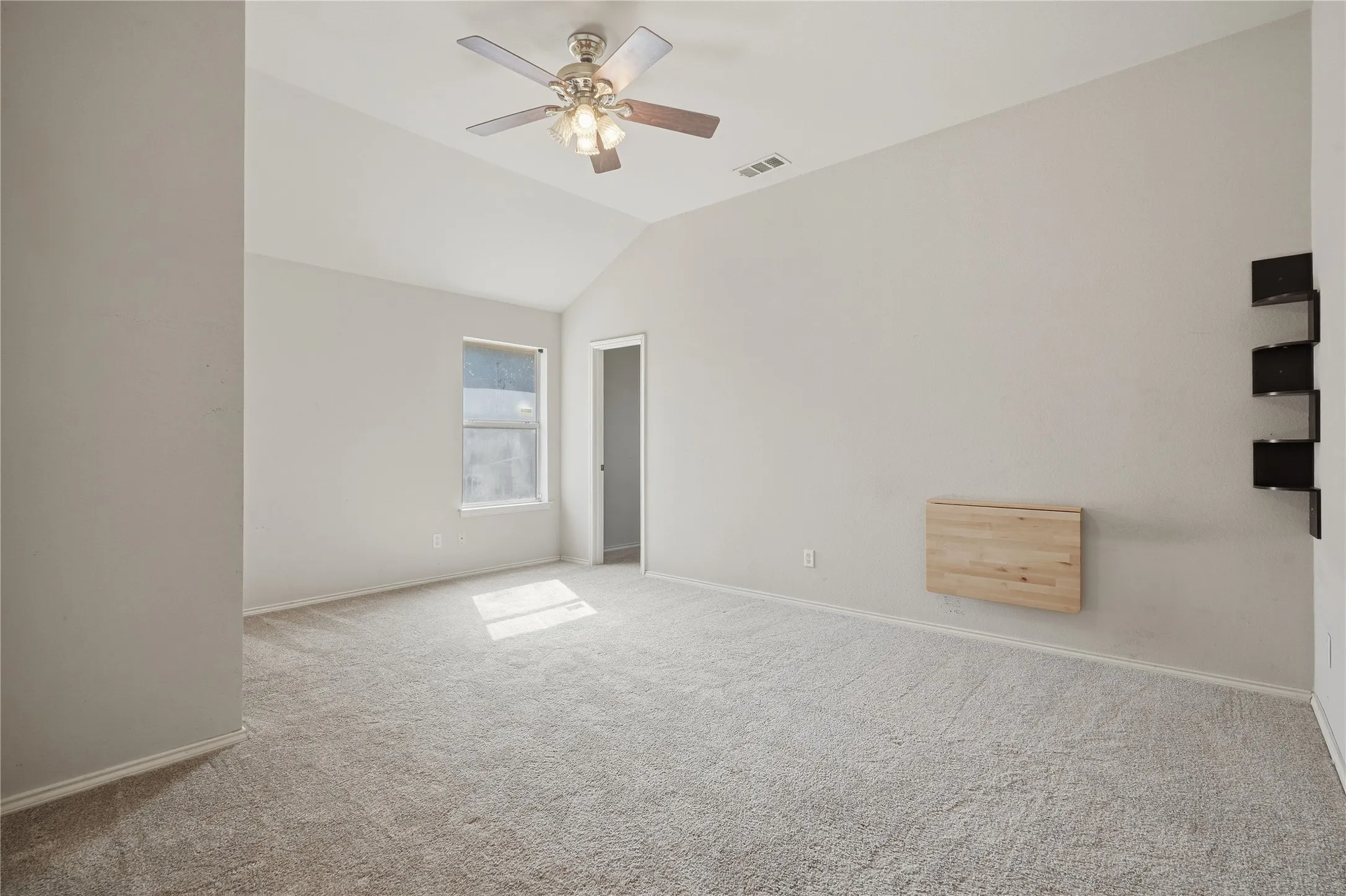 Vaulted ceiling with a ceiling fan, light-colored carpet flooring, and a window for natural light