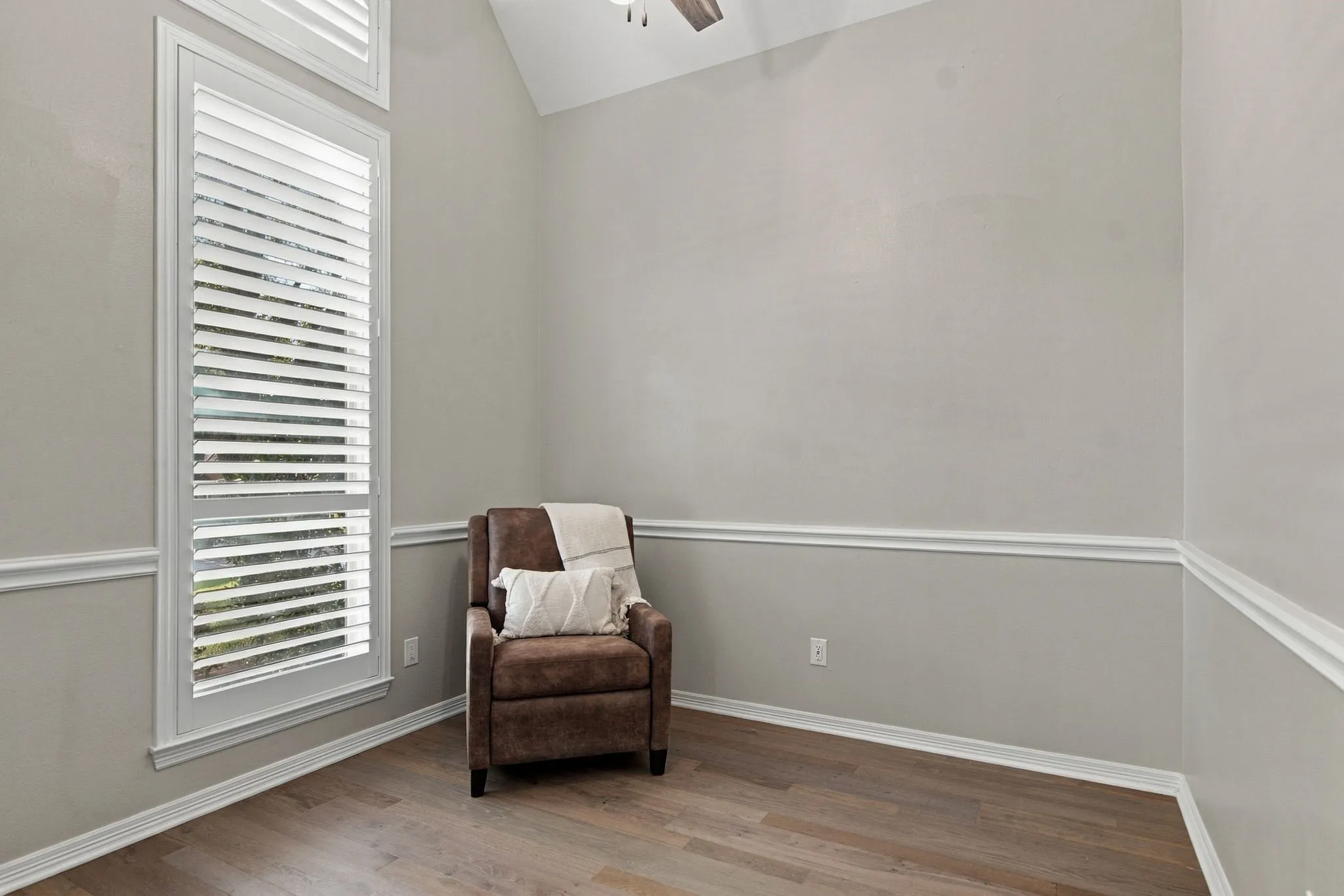 Off of the primary suite, an office features a vaulted ceiling, wood floor, tall windows with plantation shutters, and crown molding.