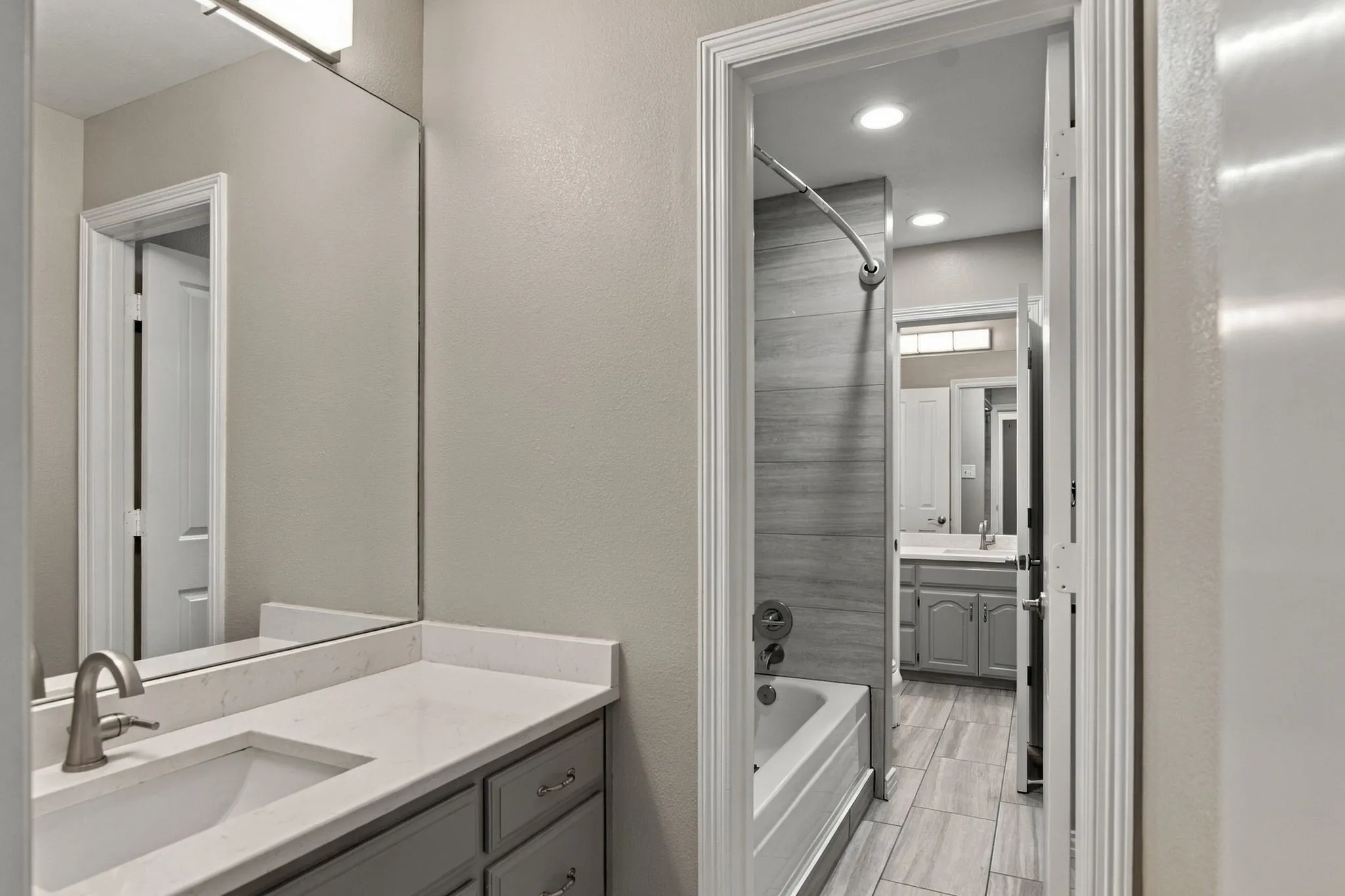 Upstairs jack and jill bath features separate vanities, light-toned quartz countertops,  gray cabinetry, and tile flooring.