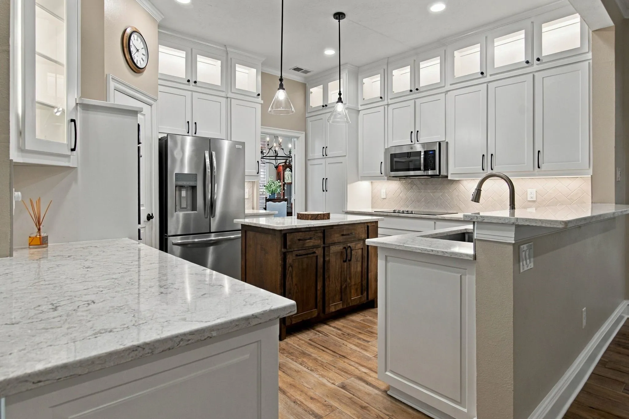 Kitchen featuring white cabinetry with glass upper doors, stainless steel appliances, a wood-finish island, and light-toned quartz countertops.