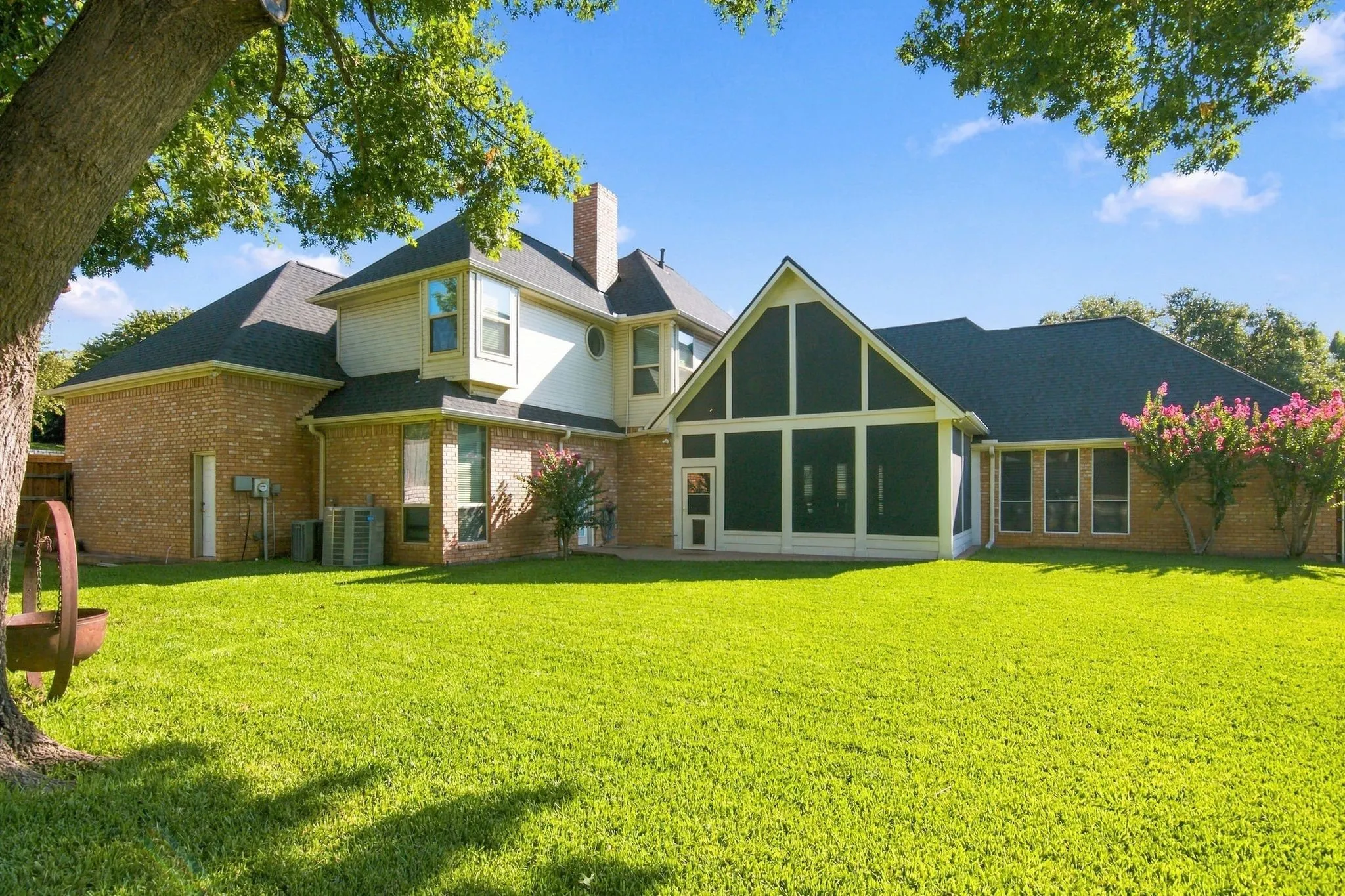 Expansive backyard featuring a manicured lawn, screened-in porch with a vaulted ceiling, brick exterior, and multiple windows.