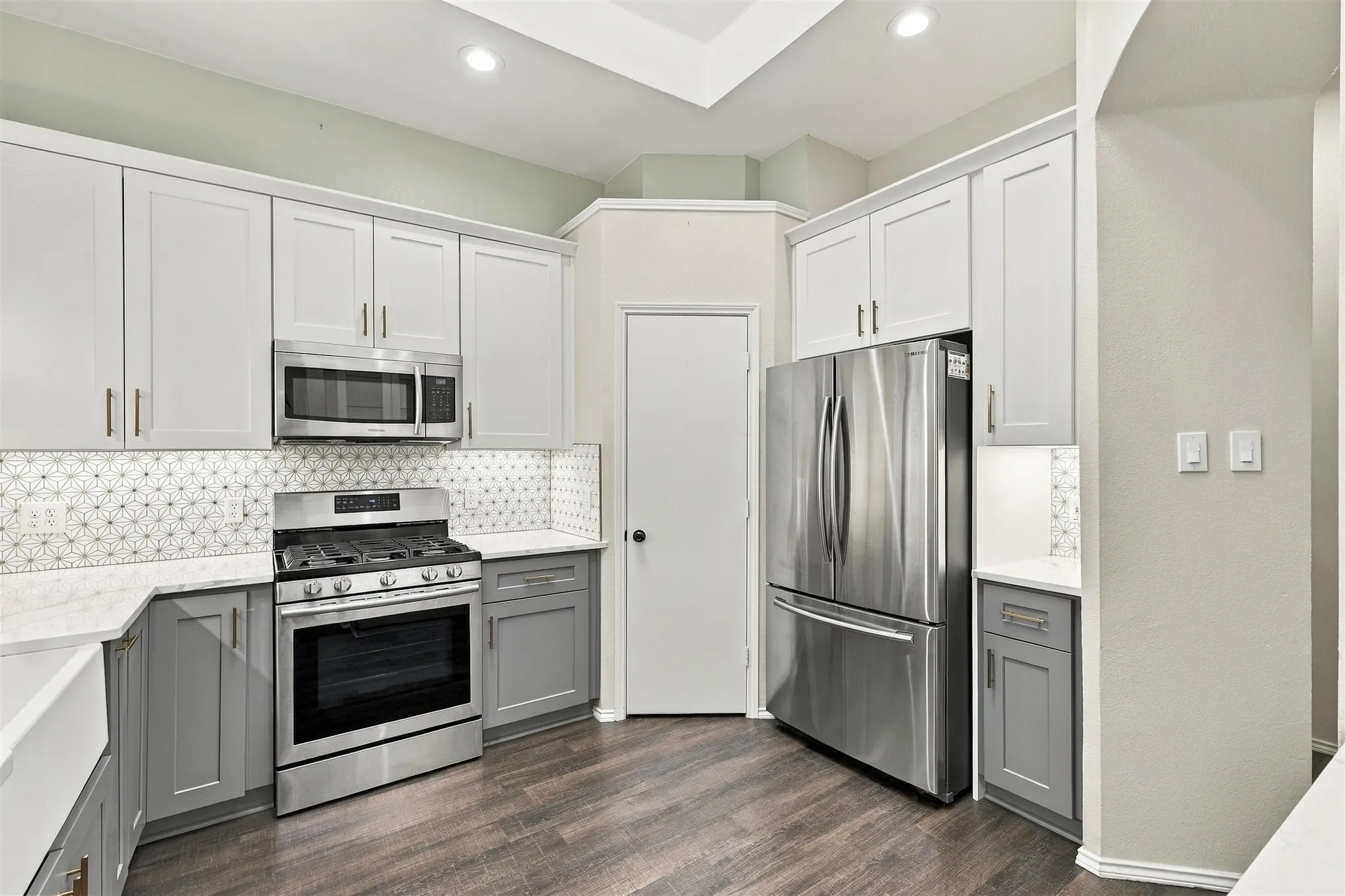 Two-tone cabinetry with white upper and gray lower cabinets, stainless steel appliances, patterned tile backsplash, white countertops, and wood-finish flooring