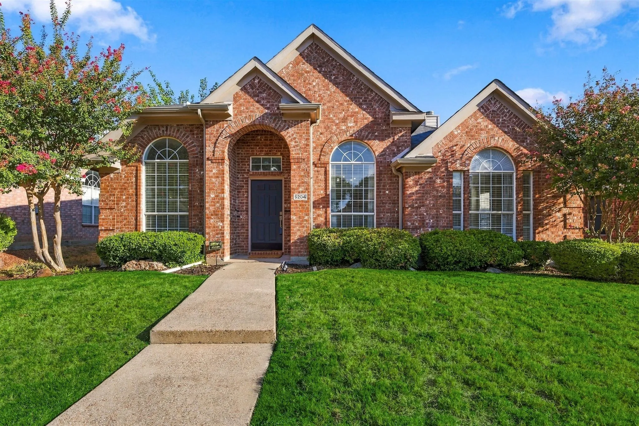 Brick facade residence with arched windows, prominent gables, and a concrete walkway