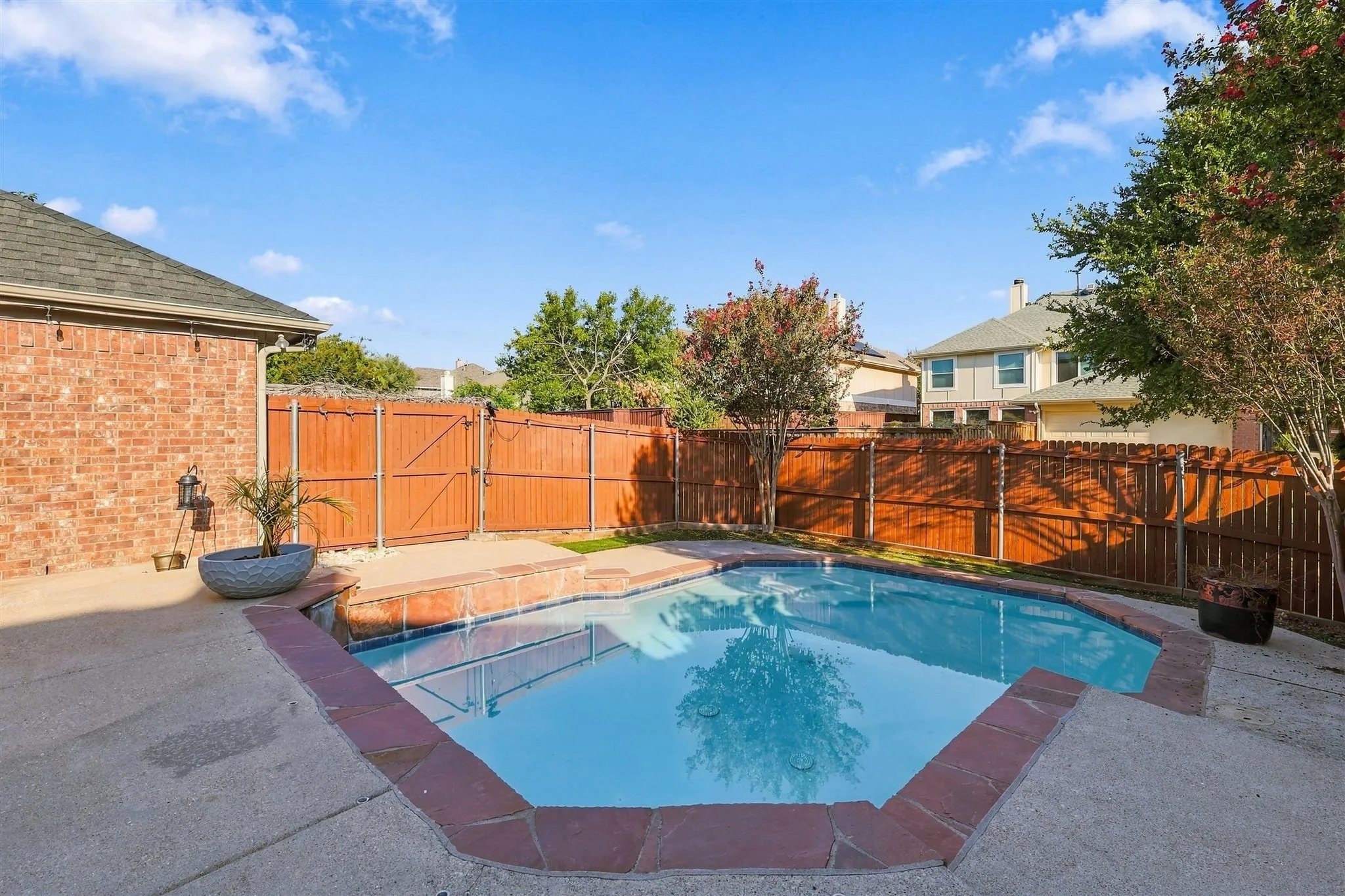 Backyard featuring a swimming pool with concrete decking, a brick house exterior, and a wooden privacy fence