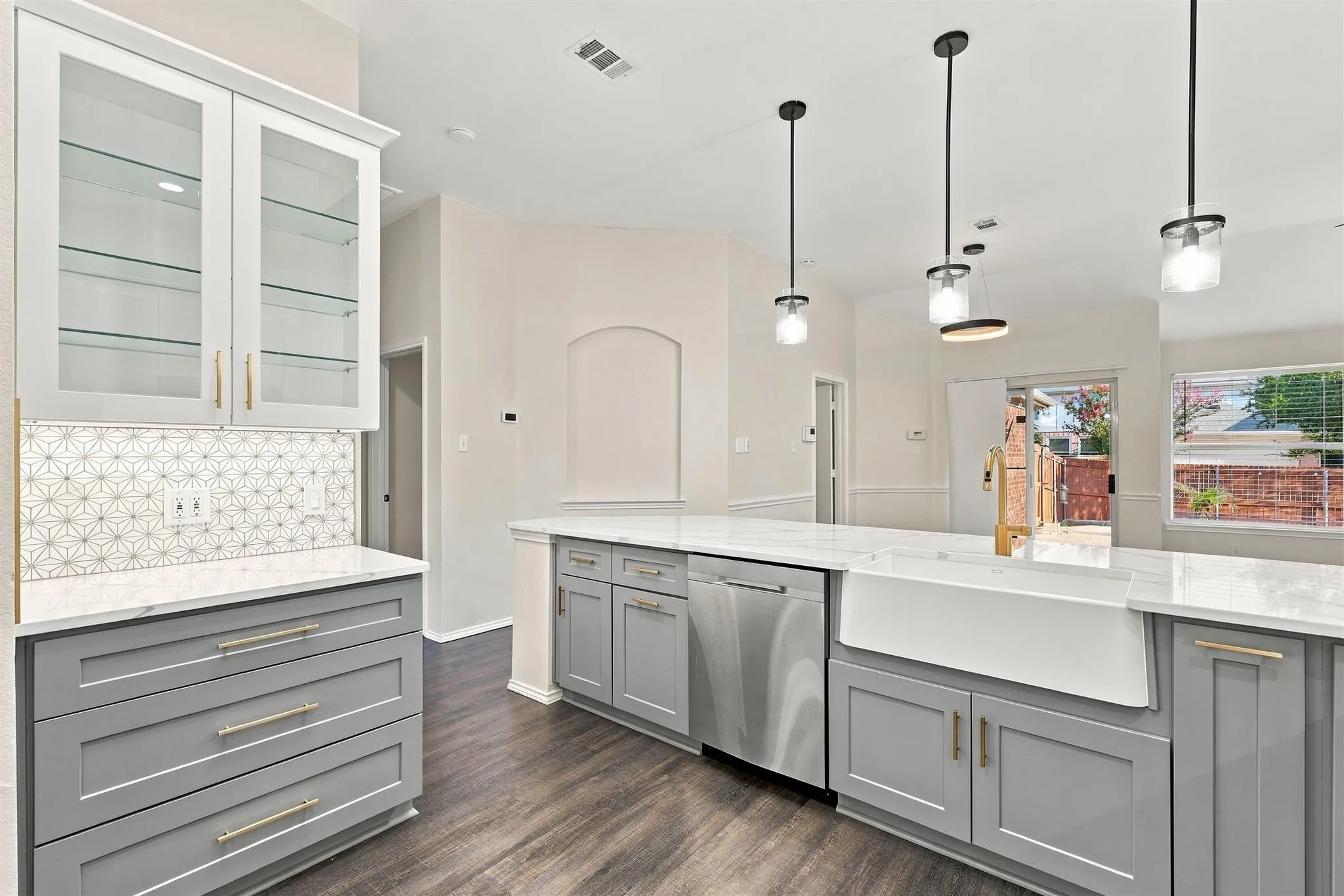 Modern kitchen featuring light gray cabinetry, white countertops, glass-front upper cabinets, a farmhouse sink, and stainless steel appliances