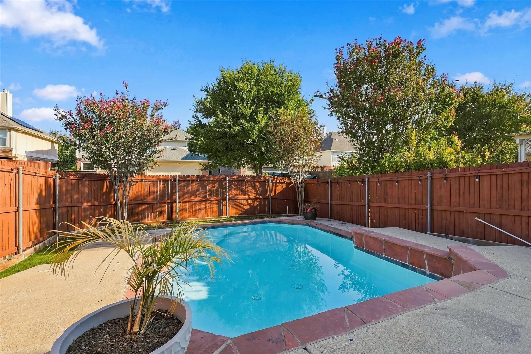 Private backyard oasis featuring a built-in swimming pool with a surrounding concrete patio, wood privacy fencing, and mature landscaping