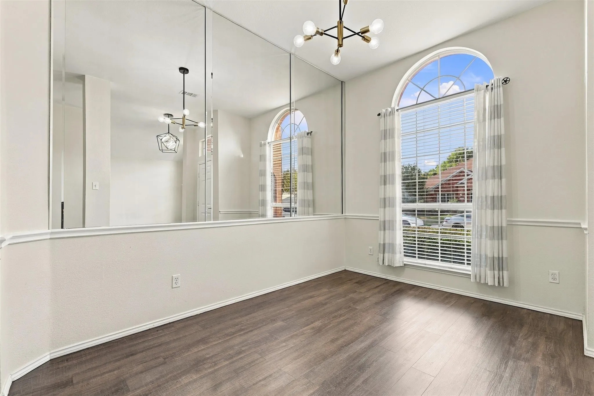 Wood-finish flooring, a contemporary chandelier, and a large arched window with blinds