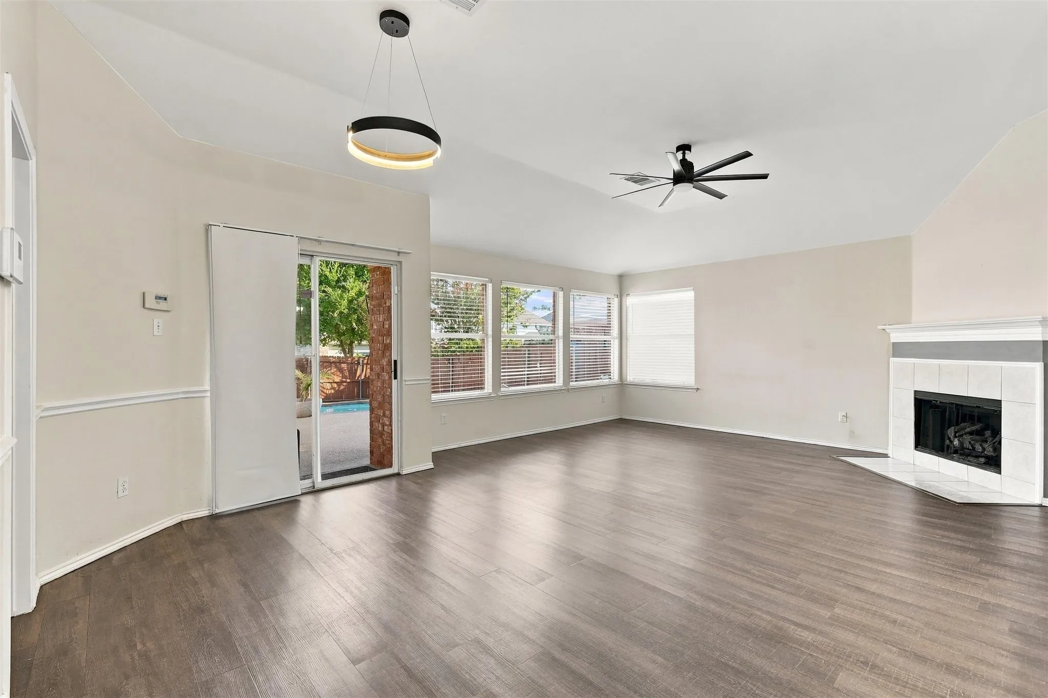 Spacious room featuring wood-finish flooring, a contemporary fireplace with a tile surround, and multiple windows with horizontal blinds