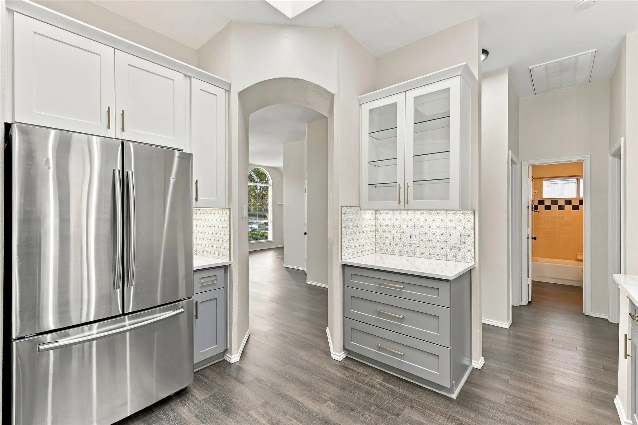 Stainless steel French door refrigerator, white upper cabinetry, glass-front display cabinet, gray lower cabinetry, and wood-finish flooring