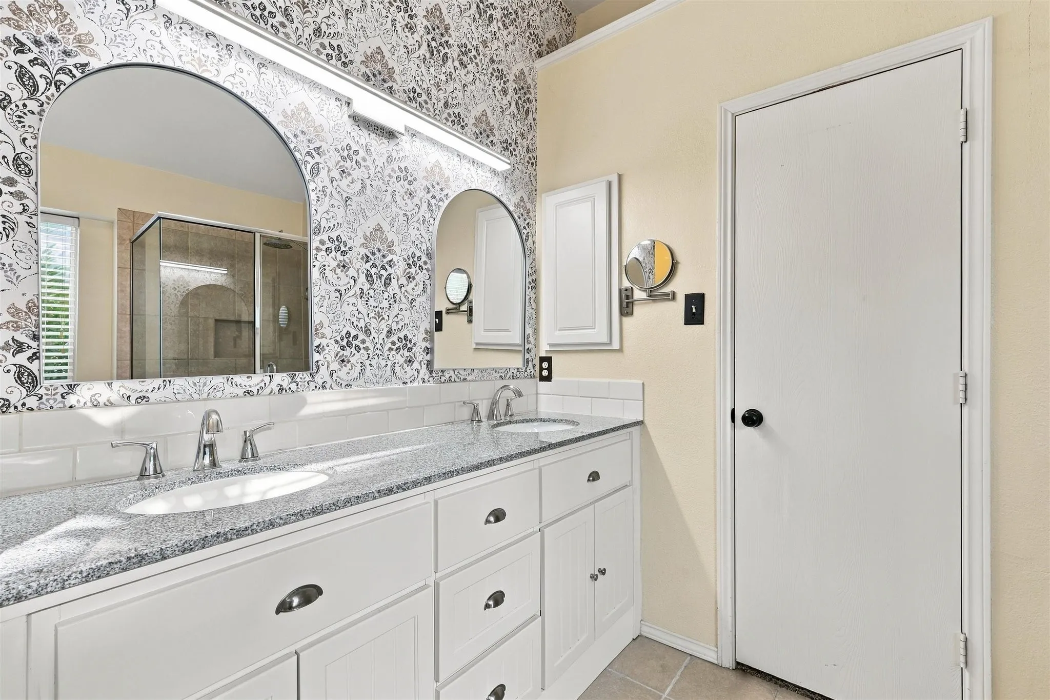 Dual arched mirrors with integrated lighting above a double vanity with stone-finish countertop