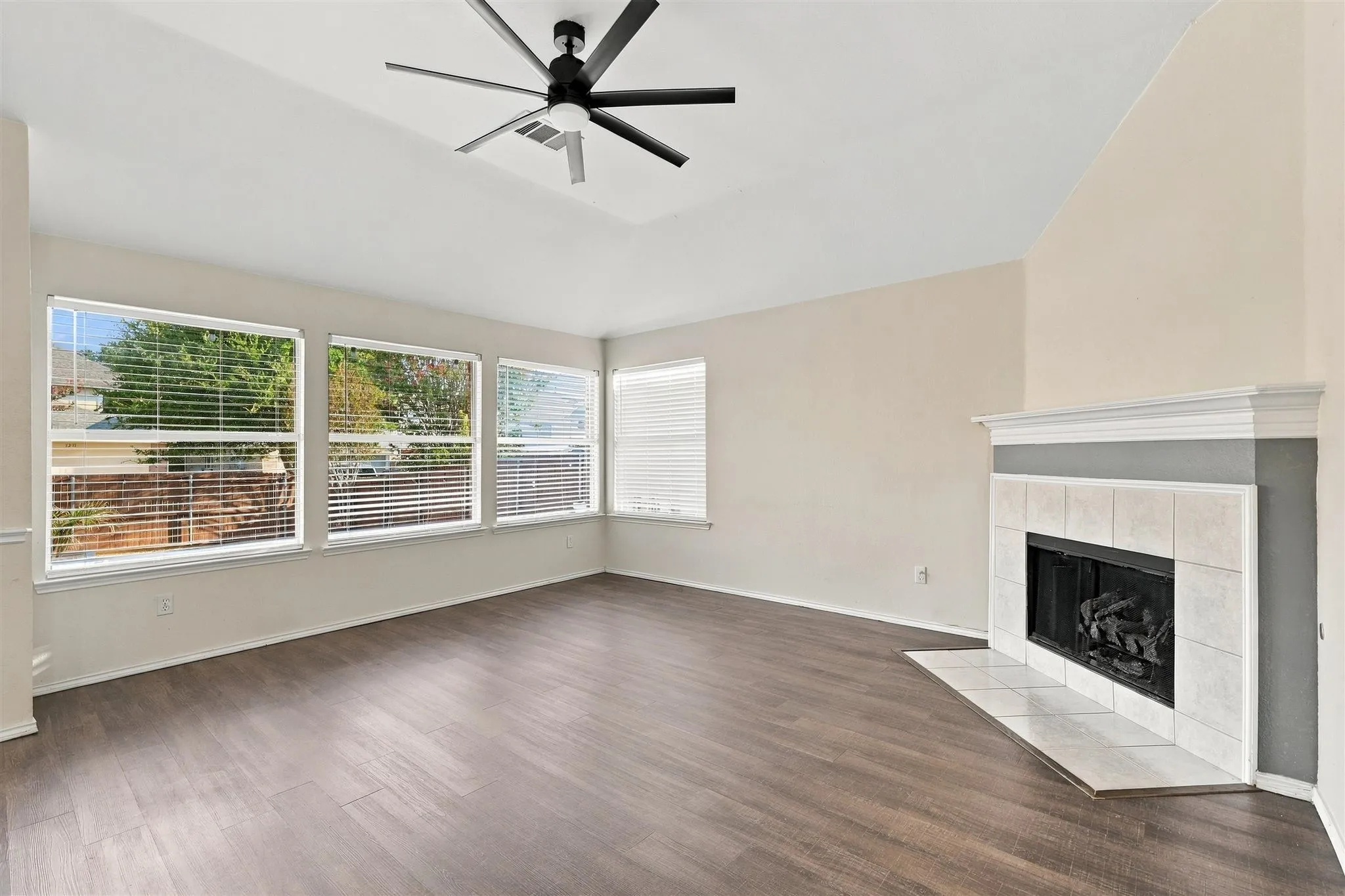 Tray ceiling with a ceiling fan, wood-finish flooring, multiple windows with blinds, and a fireplace with a white mantel and tiled surround