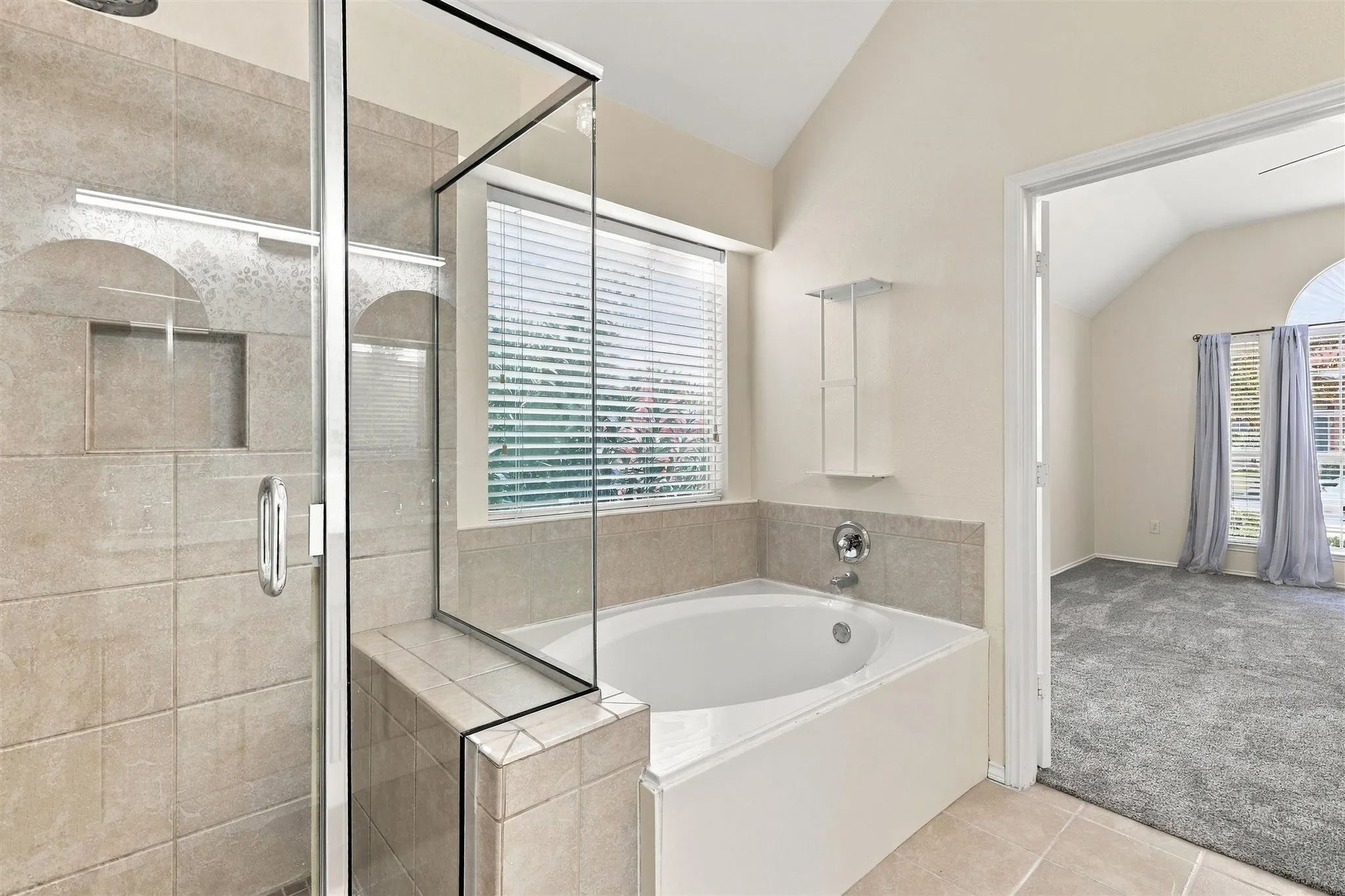 Glass-enclosed shower with a built-in niche, separate soaking tub, and tile flooring