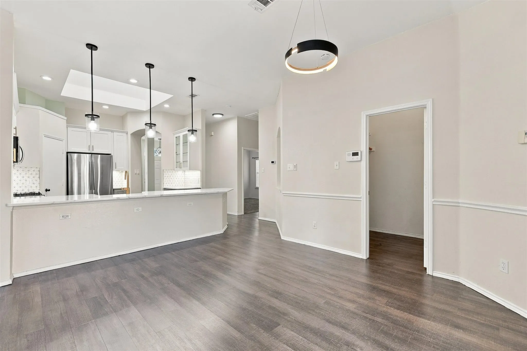 Wood-finish flooring throughout, white kitchen cabinetry, stainless steel refrigerator, white quartz countertops, and a modern circular chandelier