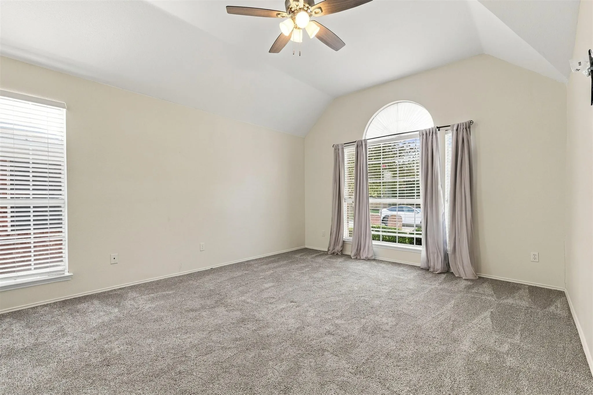 Vaulted ceiling featuring a ceiling fan with integrated lighting, arched window, and carpet flooring