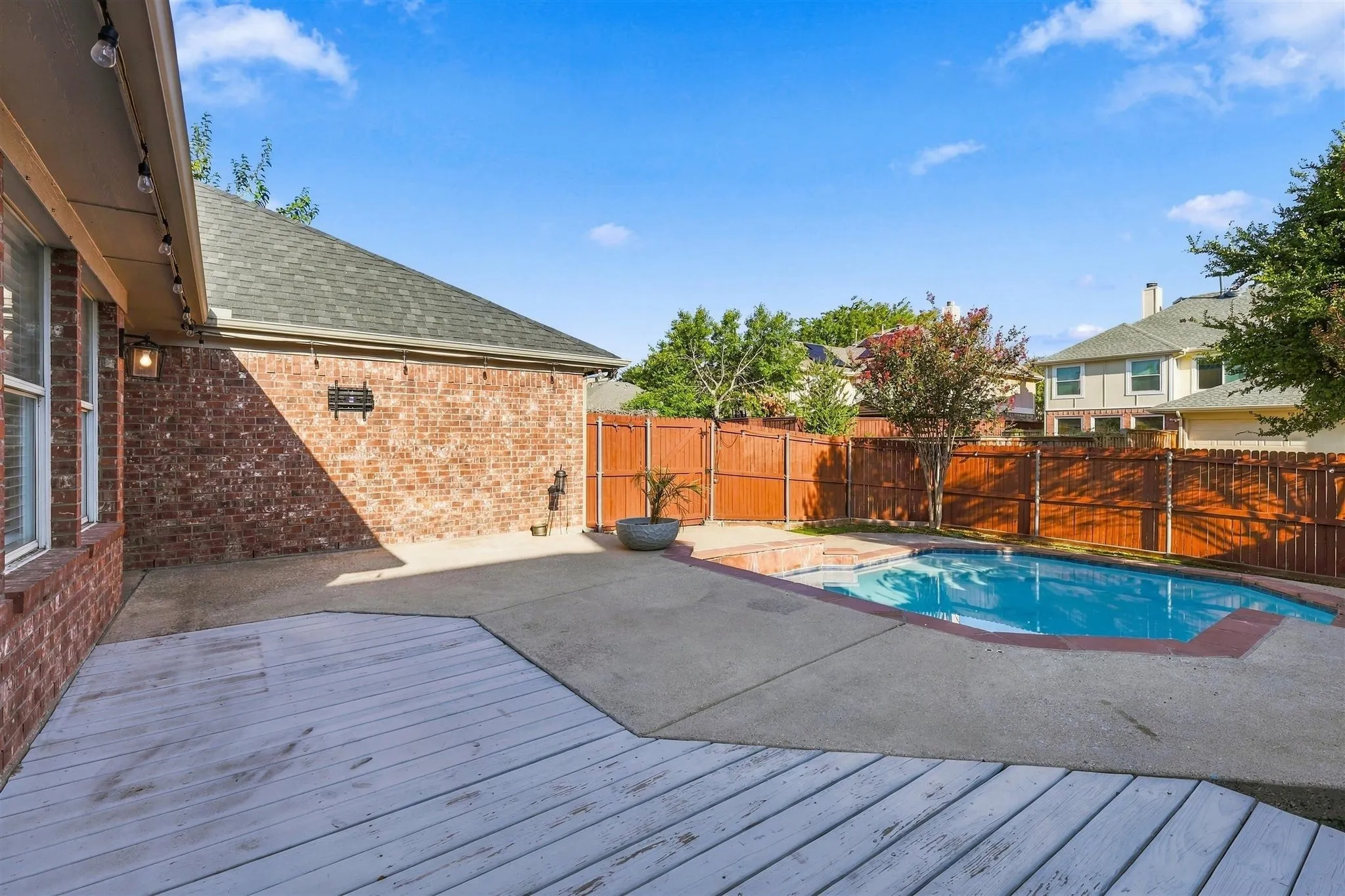 Exterior brick siding with an in-ground swimming pool, concrete patio, and a wood-finish deck
