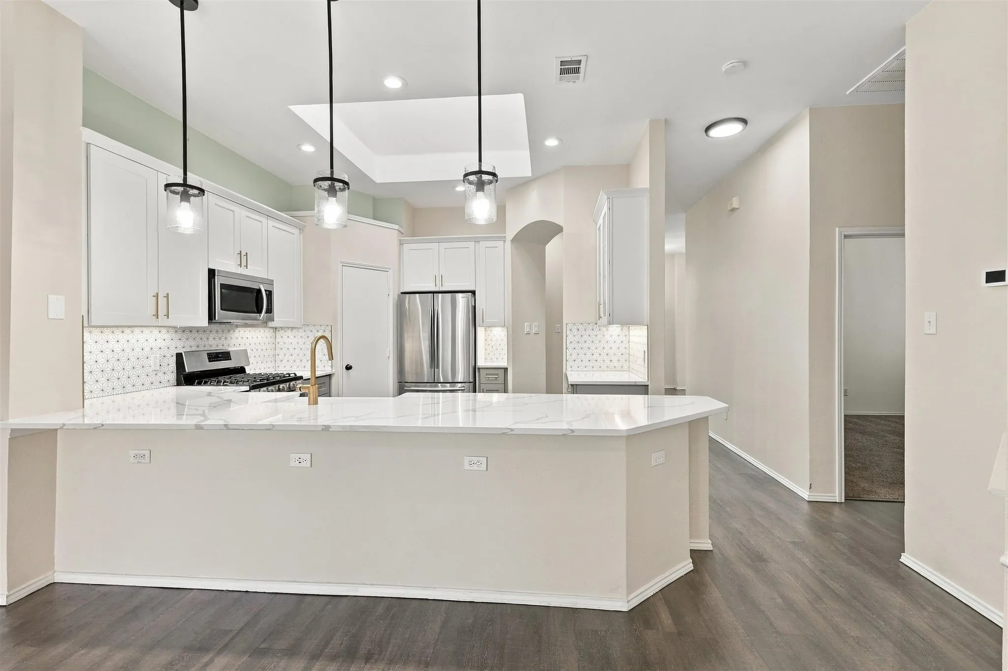 Kitchen featuring a large central island, stainless steel appliances, white cabinetry with gold-finish hardware, a patterned tile backsplash, and wood-finish flooring