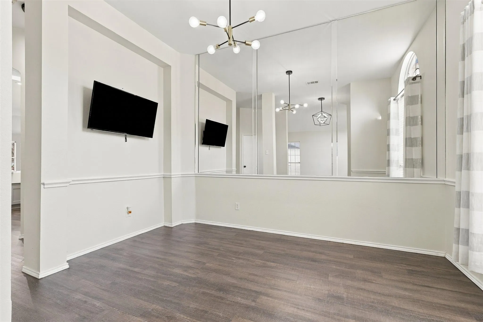 Wood-finish flooring, two-tone wall treatment, decorative chair rail, built-in wall mirrors, and a modern chandelier
