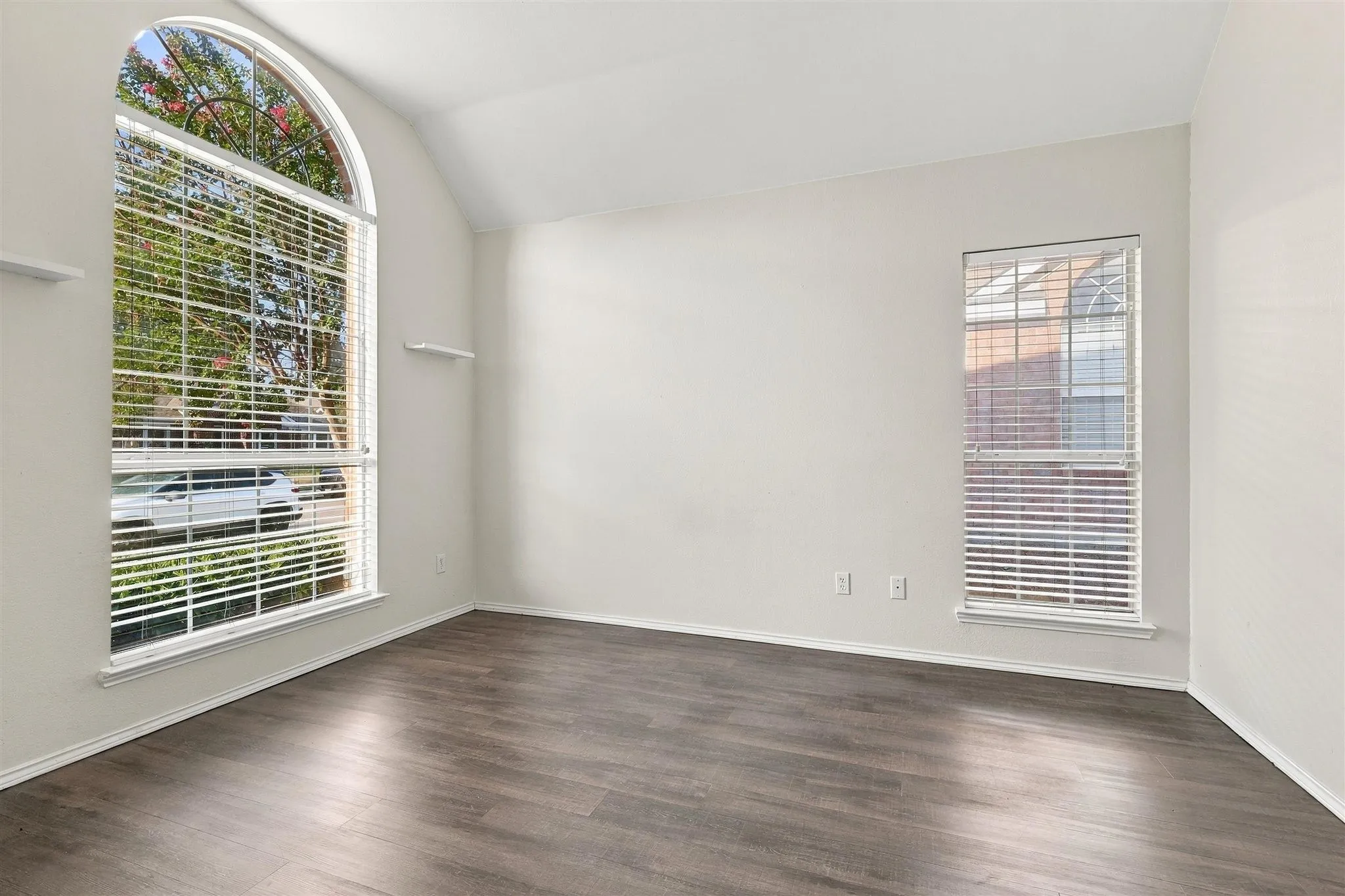 Vaulted ceiling with wood-finish flooring, featuring a large arched window and additional window with blinds