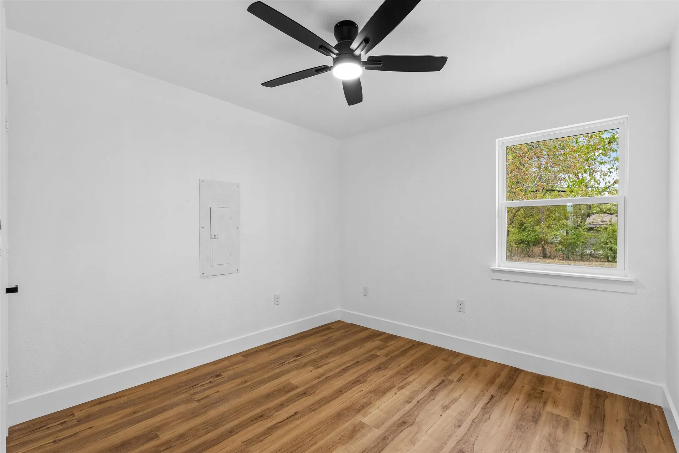 Bright room featuring wood-finish flooring, a contemporary ceiling fan with integrated lighting, and a window with white trim