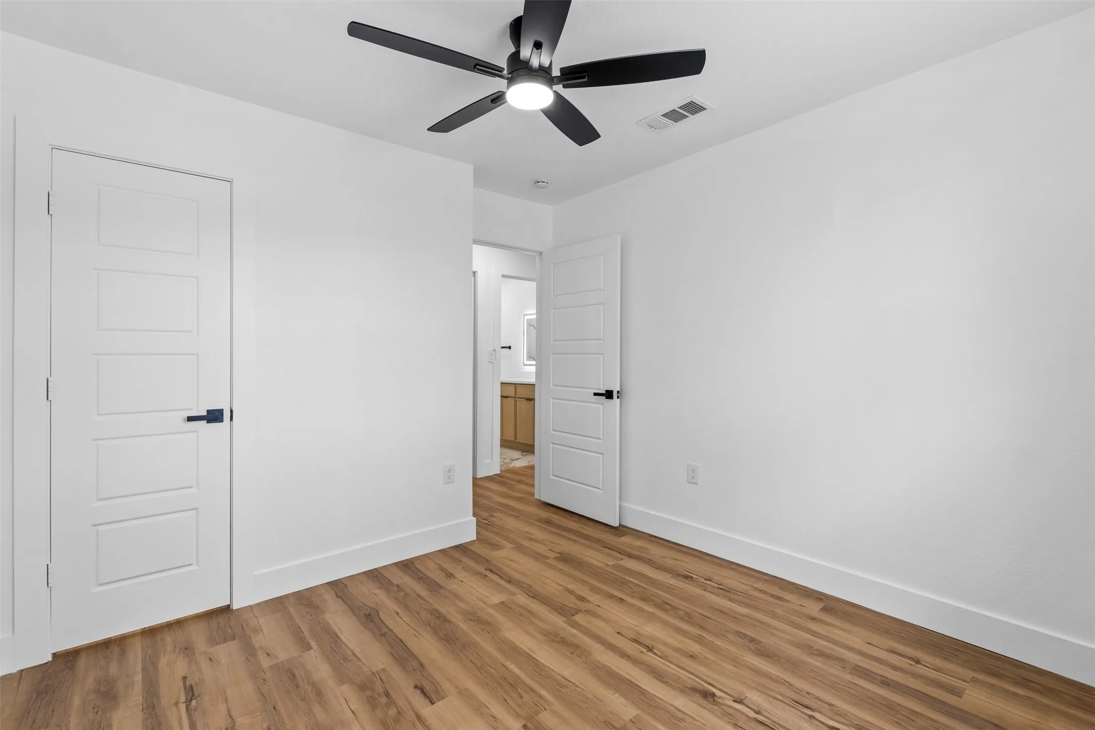 Wood-finish flooring, white walls, and a contemporary ceiling fan with integrated lighting