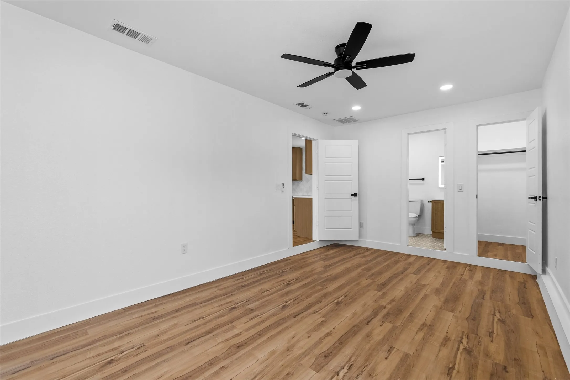 Wood-finish flooring throughout, white walls, recessed lighting, and a black ceiling fan